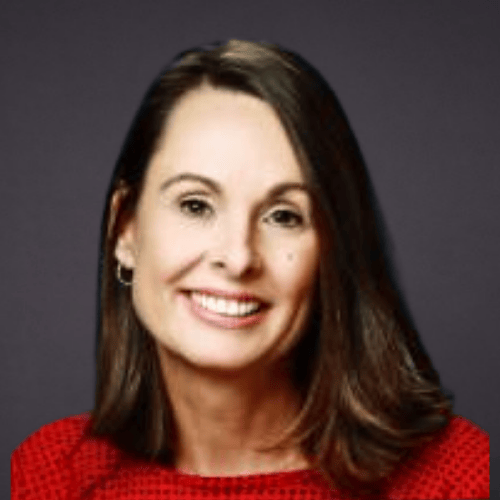 A woman with shoulder-length brown hair smiling, wearing a red top and earrings, against a dark background.