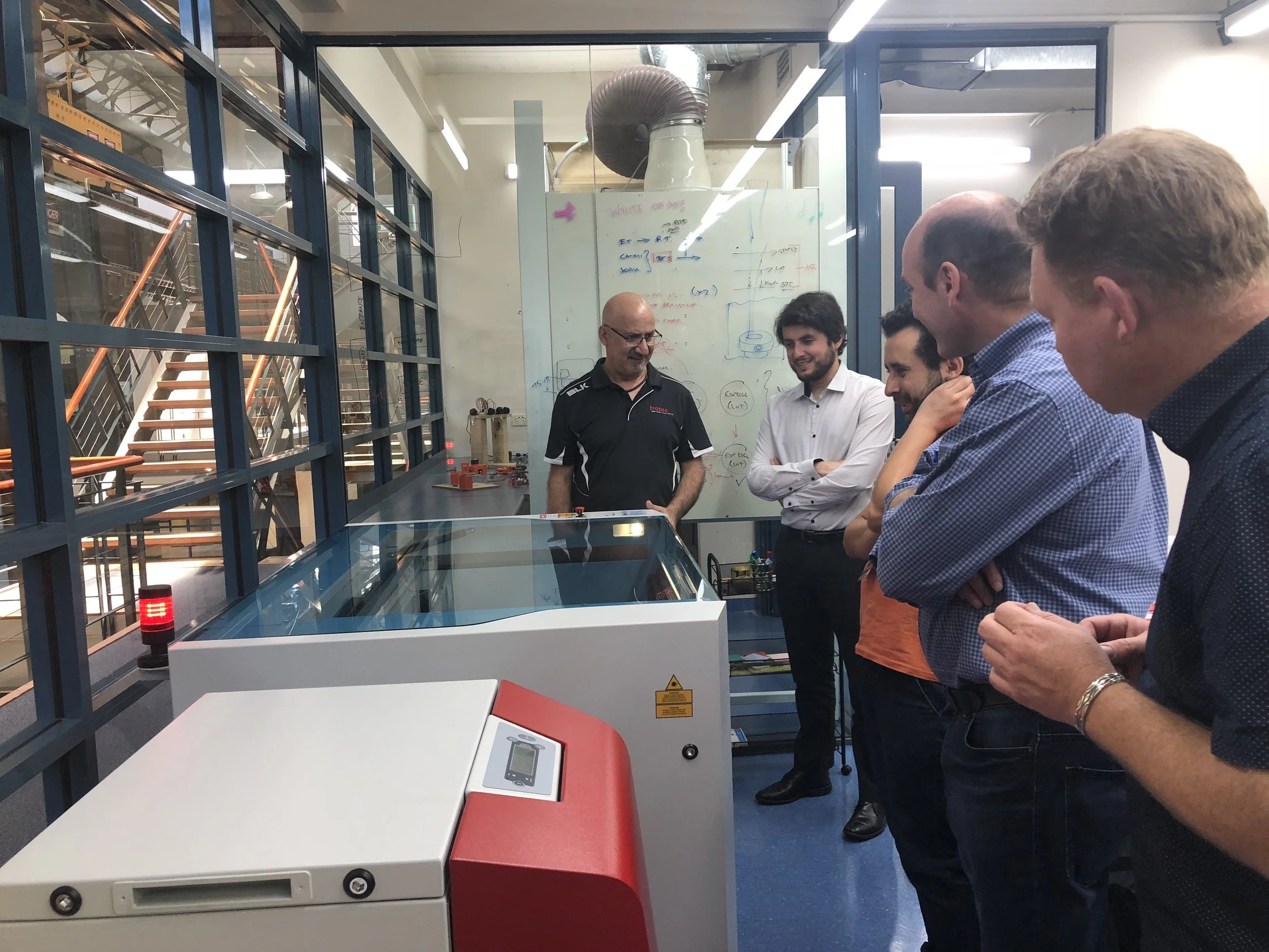 A group of people standing around the laser cutter