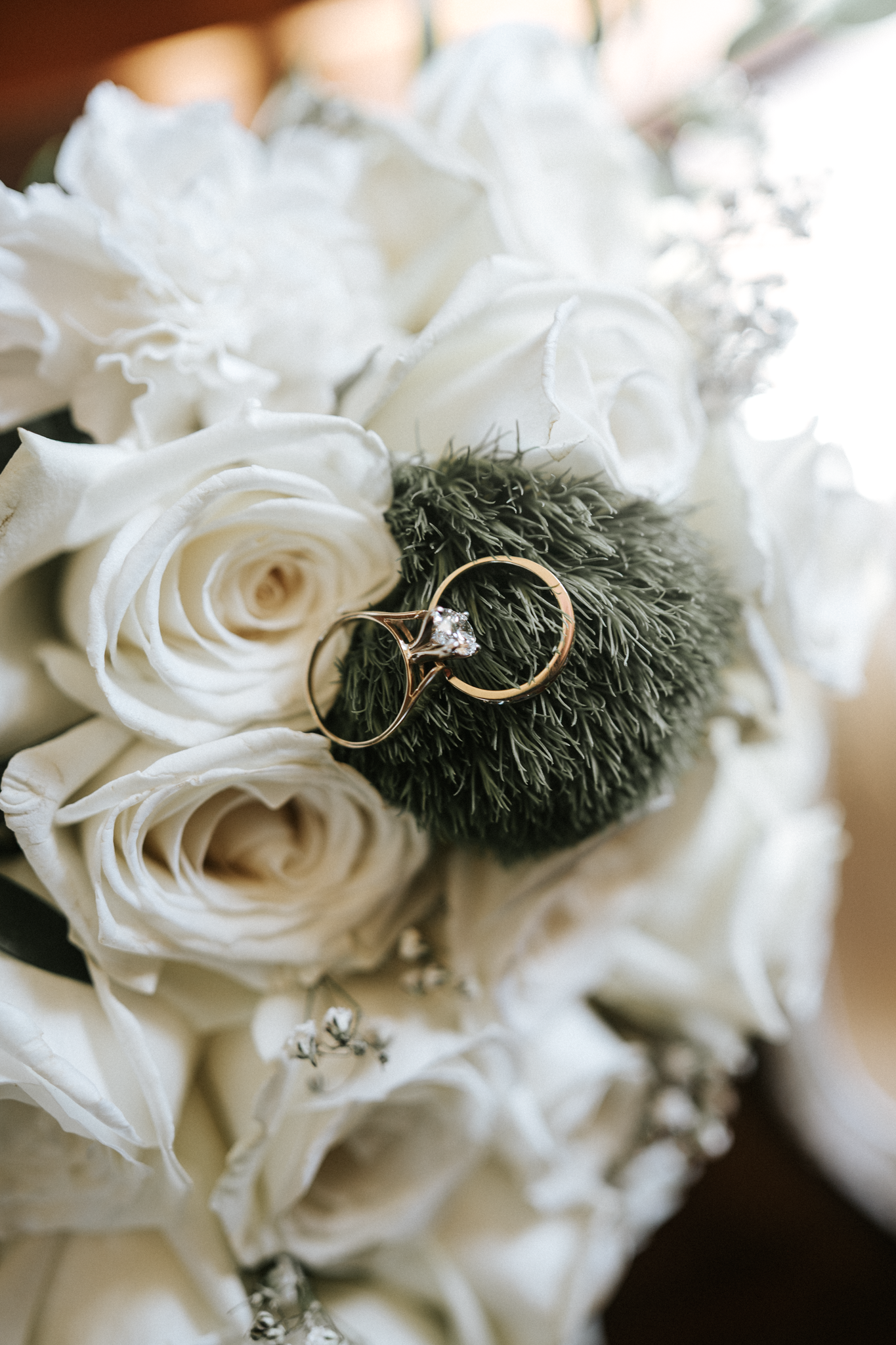 Close-up of a bouquet with white roses and green foliage, with gold wedding rings resting on the greenery.