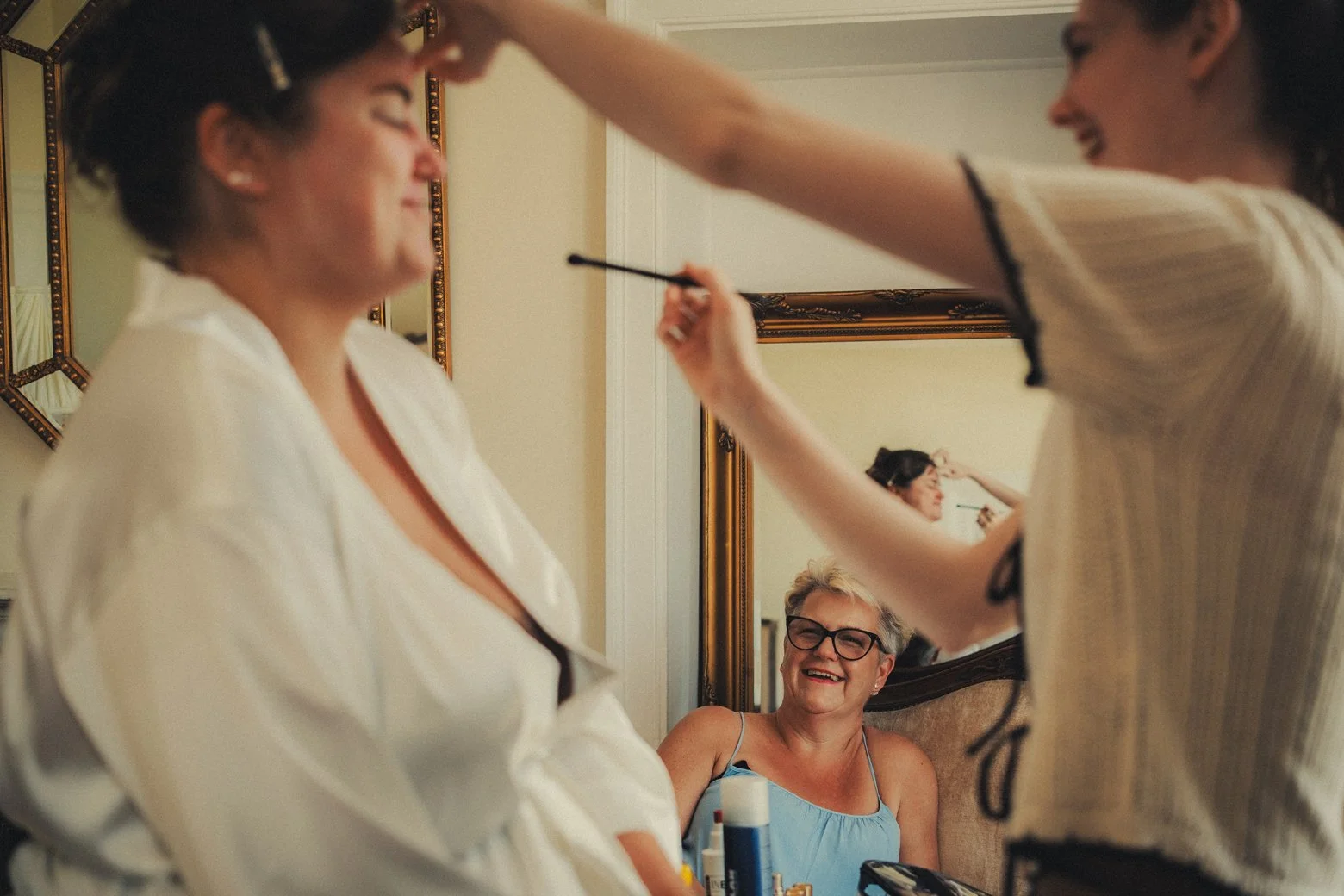 Mother joyfully watching bride getting makeup during wedding morning