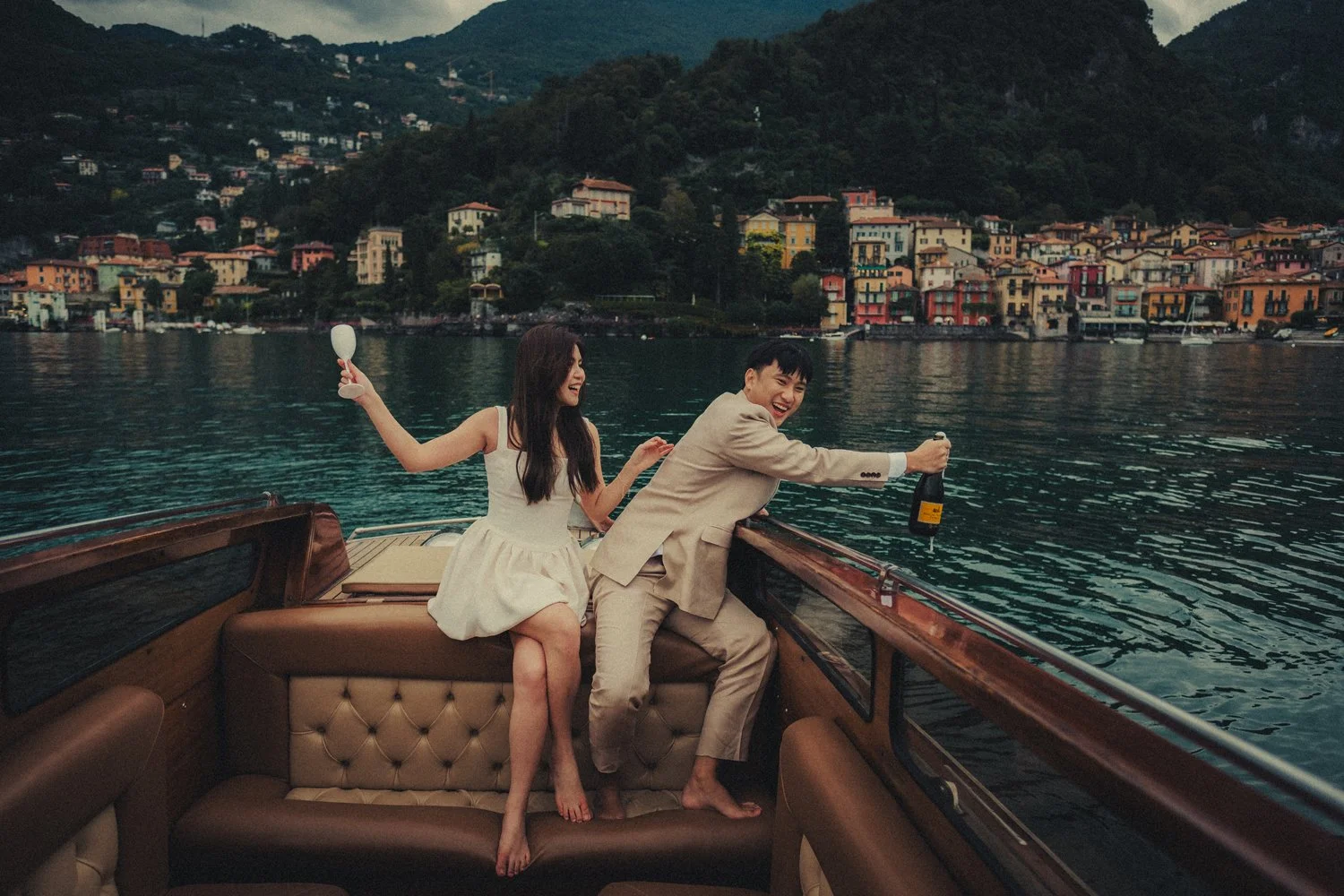 Lake Como pre-wedding photographer capturing a couple popping a bottle of champagne on a classic wooden boat.