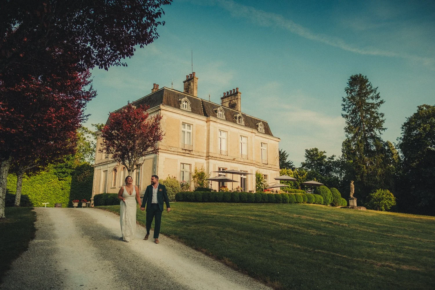 Bride and groom walking beside Château La Gauterie during a sunny Dordogne wedding in South West France