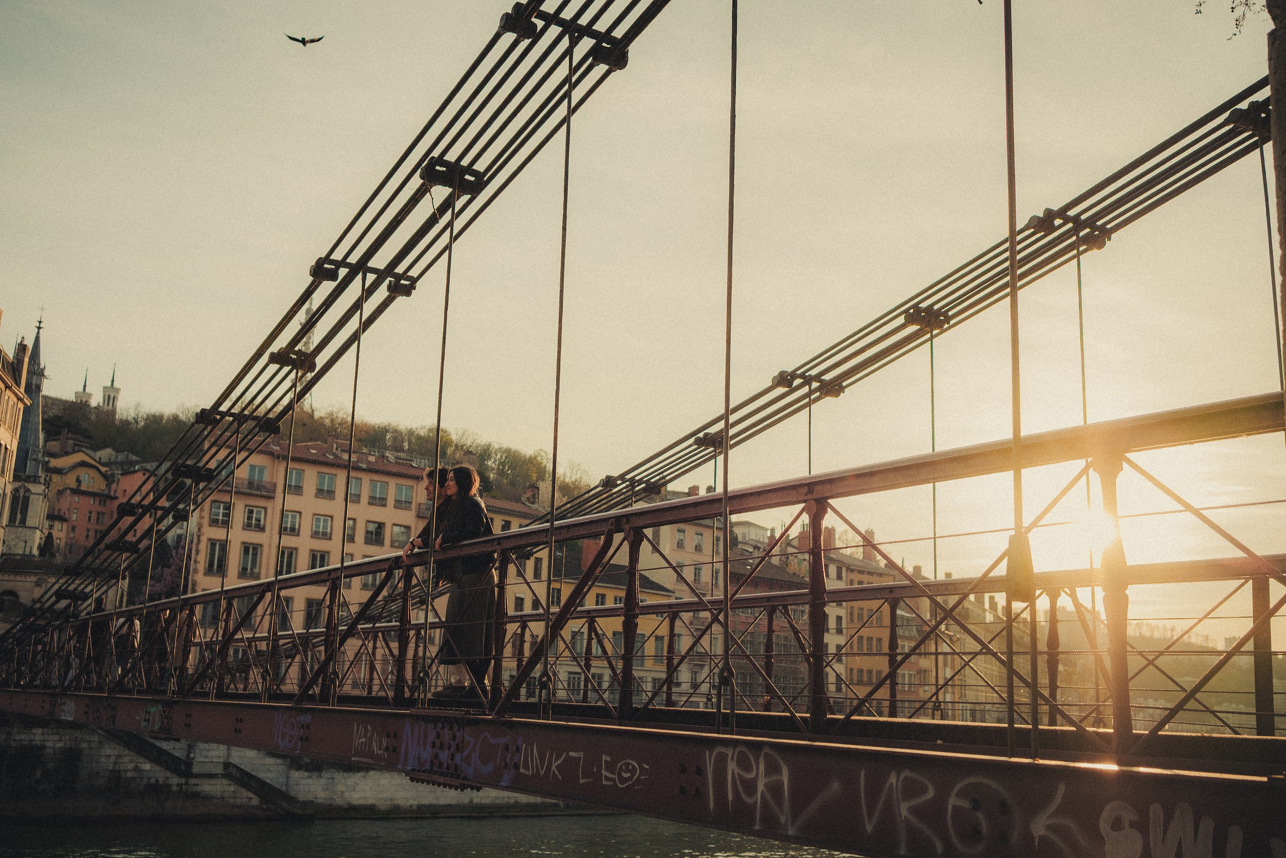 Photo large du couple sur un pont à Lyon au coucher du soleil.