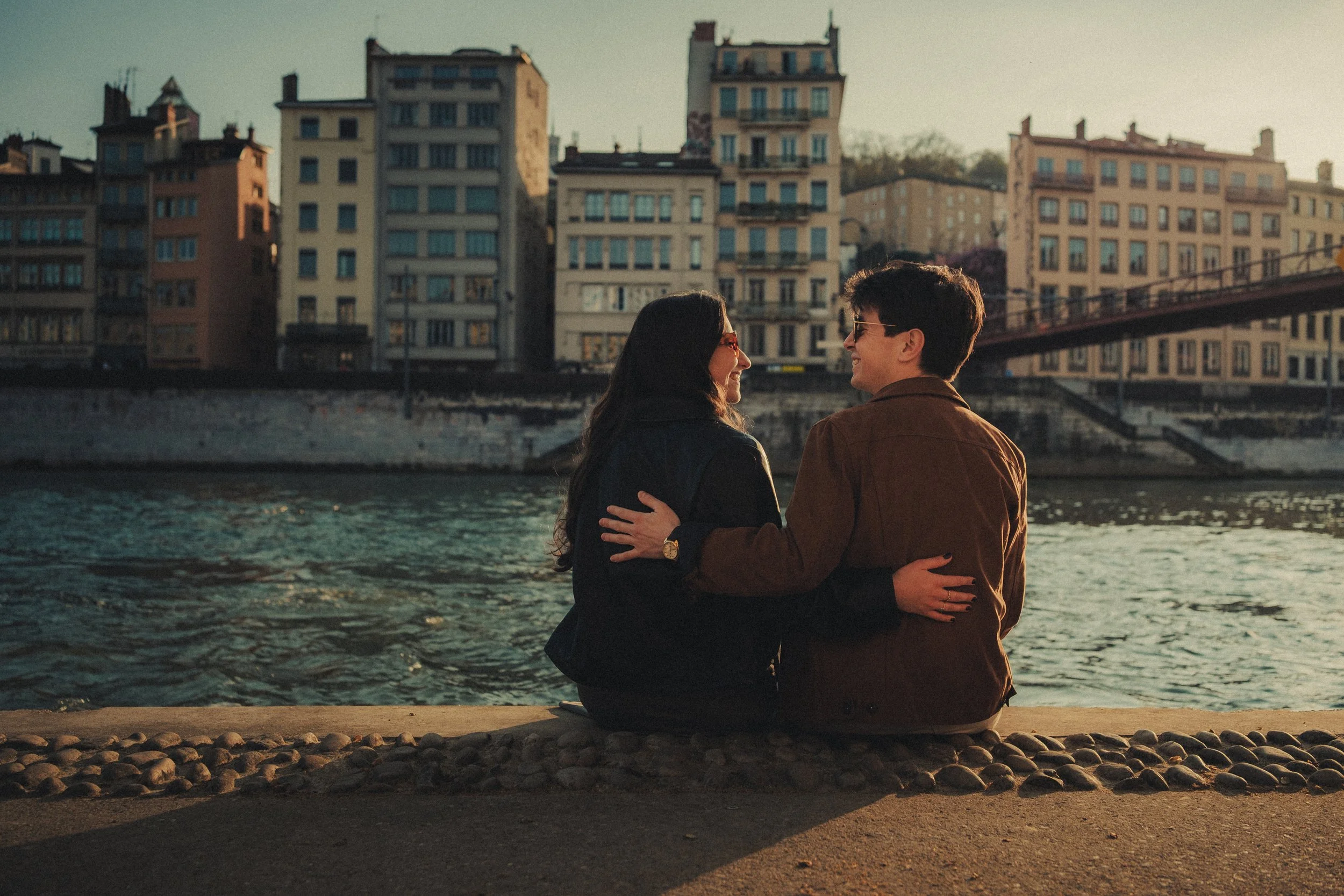 photographe engagement capturé le couple enlacé assis sur les quais de Saône à Lyon.