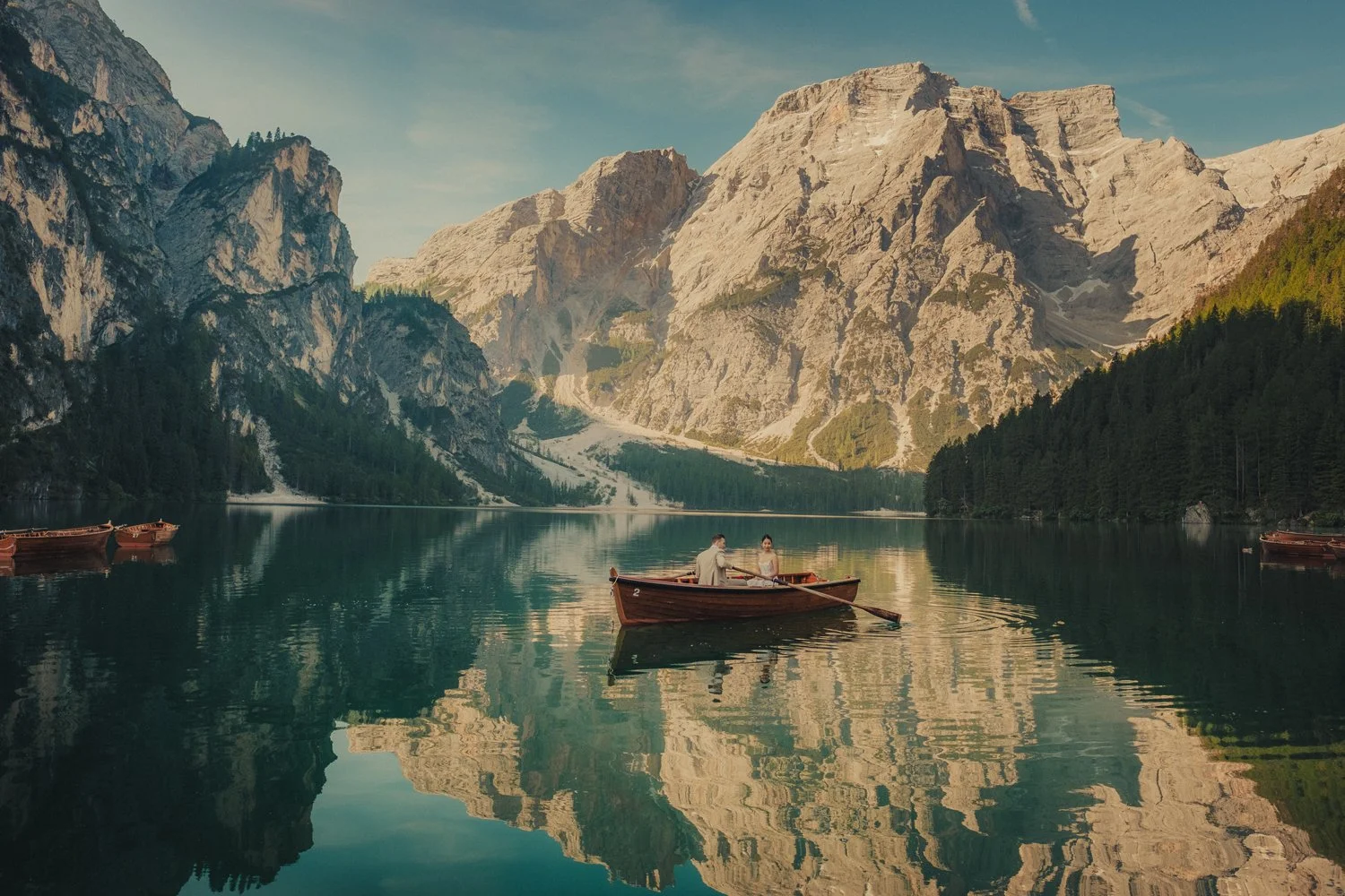 Dolomites elopement photographer capturing bride and groom rowing a wooden boat with a mountain backdrop.