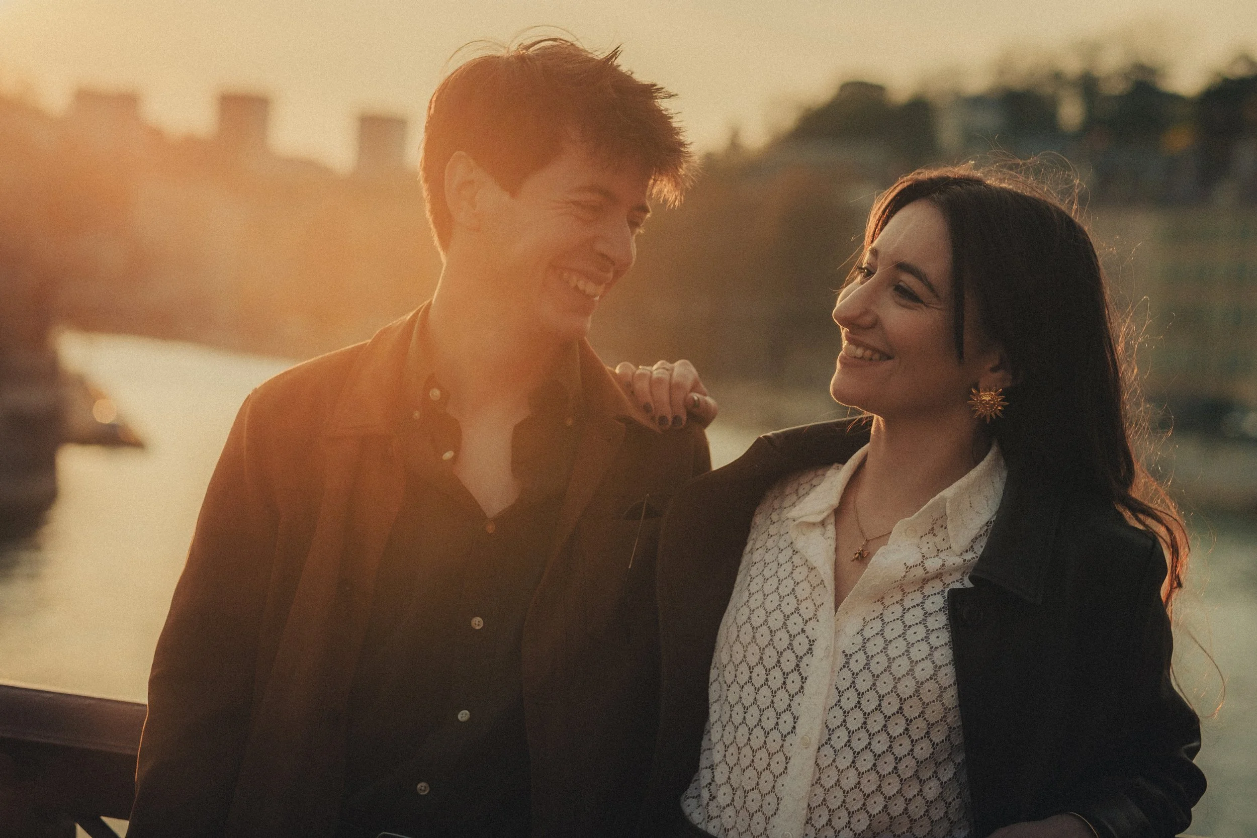 Photographe engagement capturé un couple riant sur un pont à Lyon au coucher du soleil.