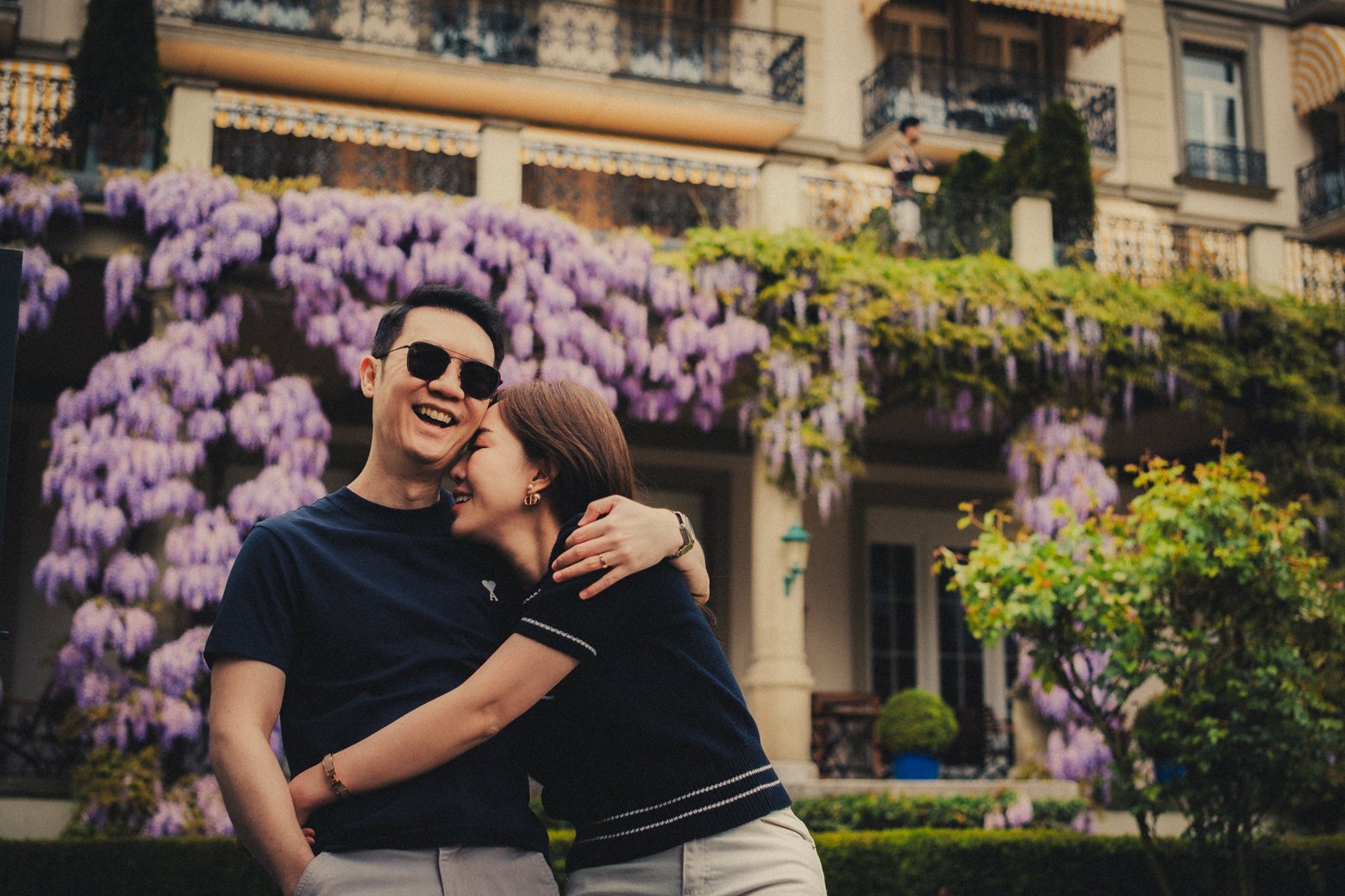 Candid portrait of a couple laughing in front of purple spring blossoms in Switzerland.