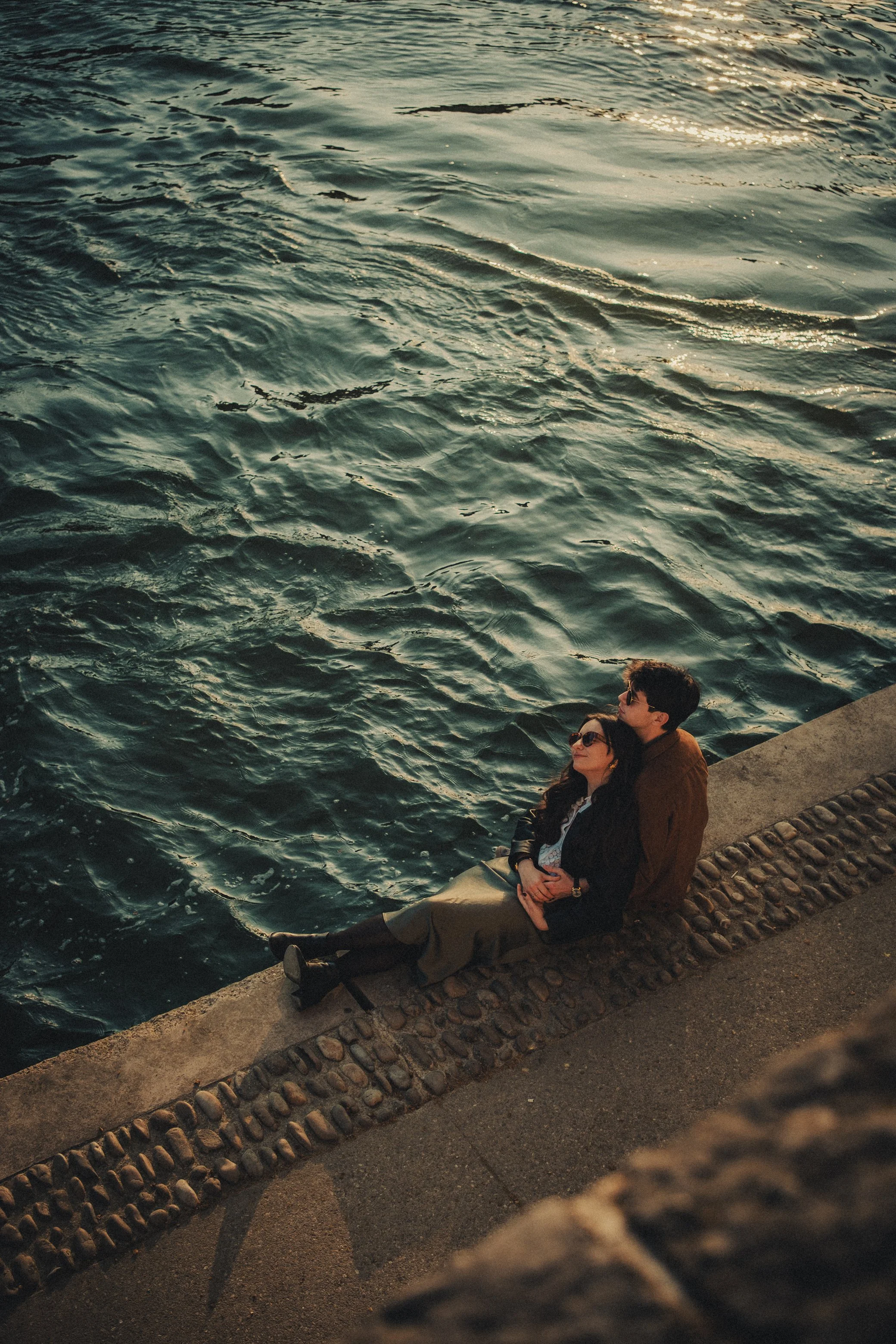 photographe engagement capturé le couple assis au bord des quais de Saône à Lyon baignés par la lumière du soleil.