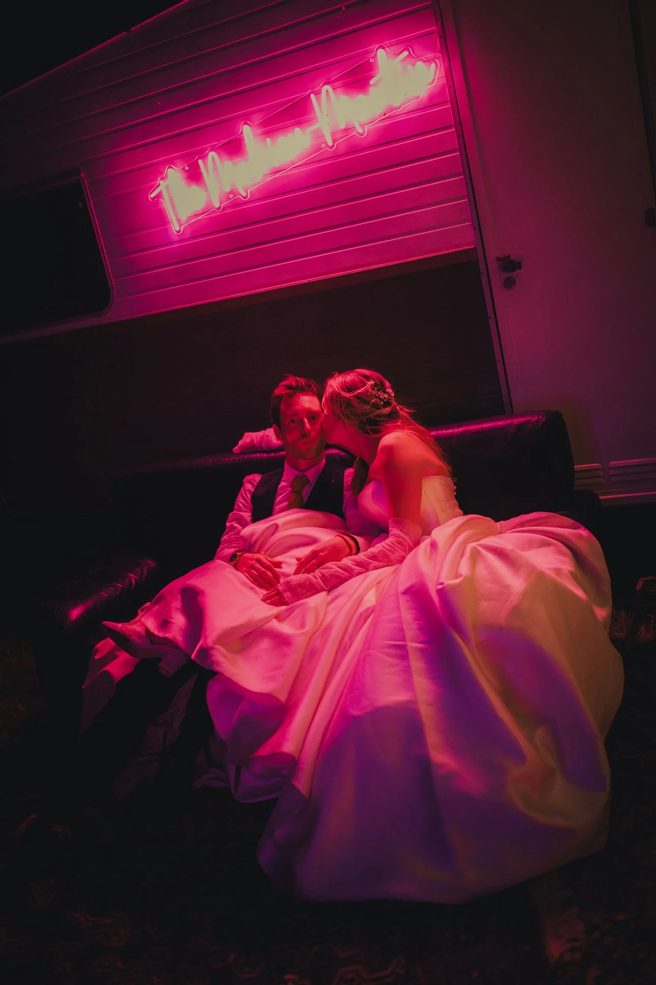 Bride kissing groom under a pink neon light at their wedding in Provence.