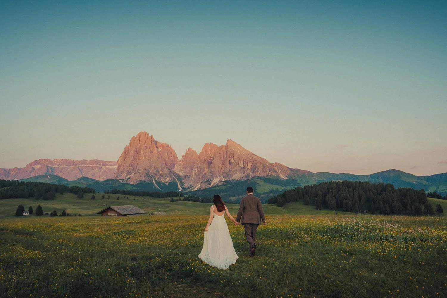 Dolomites elopement photographer capturing a couple walking with a majestic mountain as a backdrop during sunset.