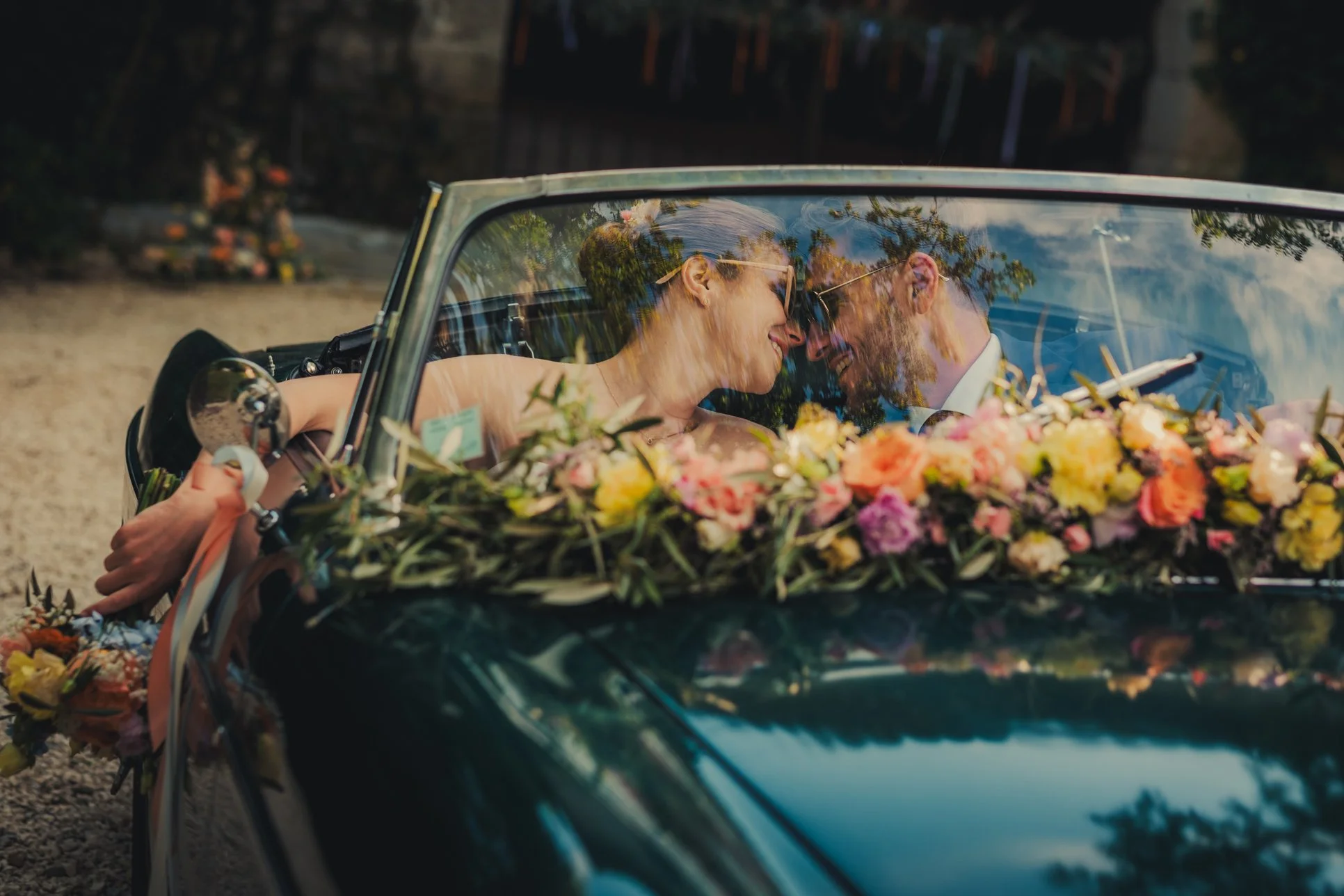 Mariés avec lunettes de soleil posant dans d’une voiture vintage décorée de fleurs au Domaine des Rives