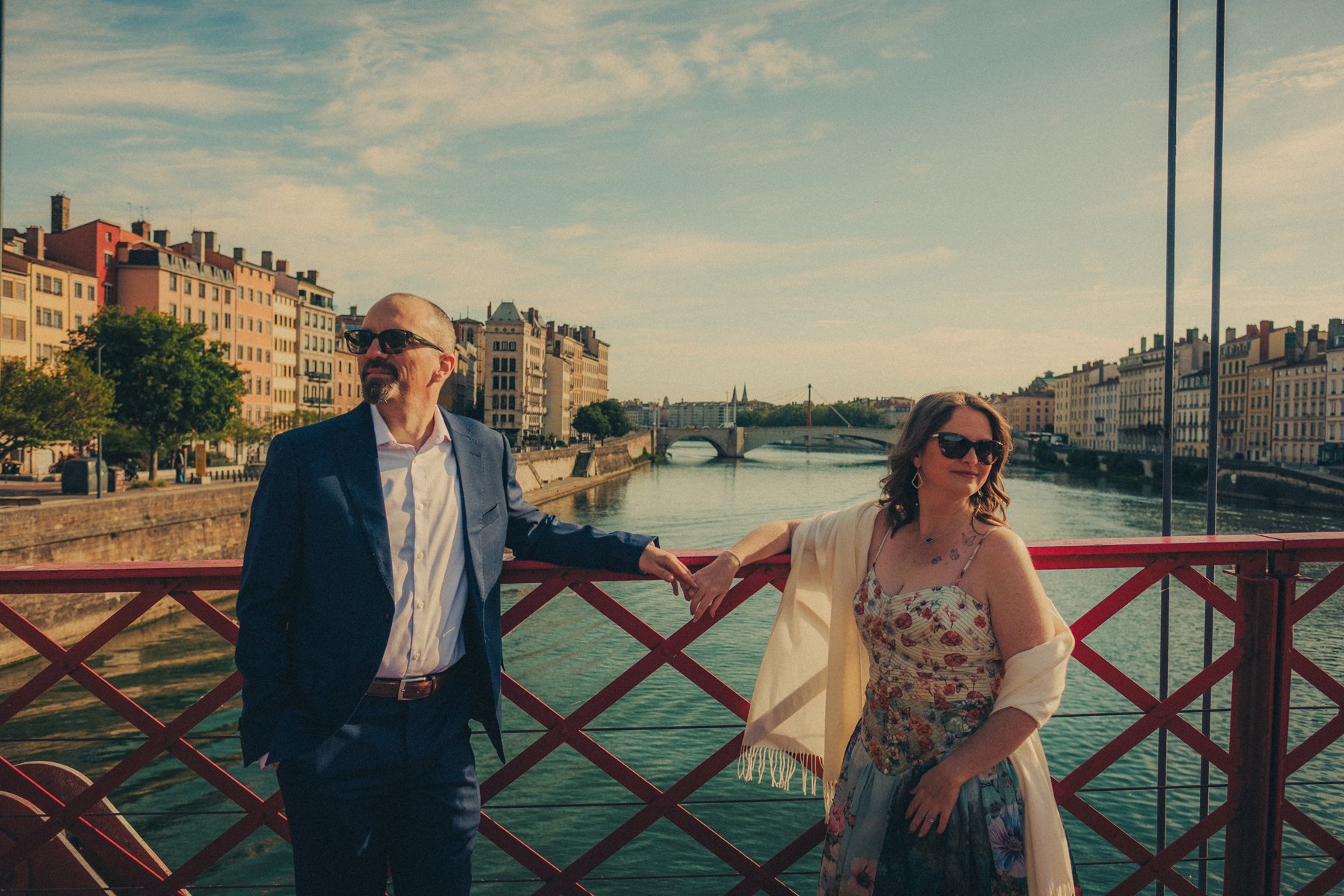 Couple with sunglasses posing and holding hands on the red bridge of Lyon after their vow renewal ceremony.
