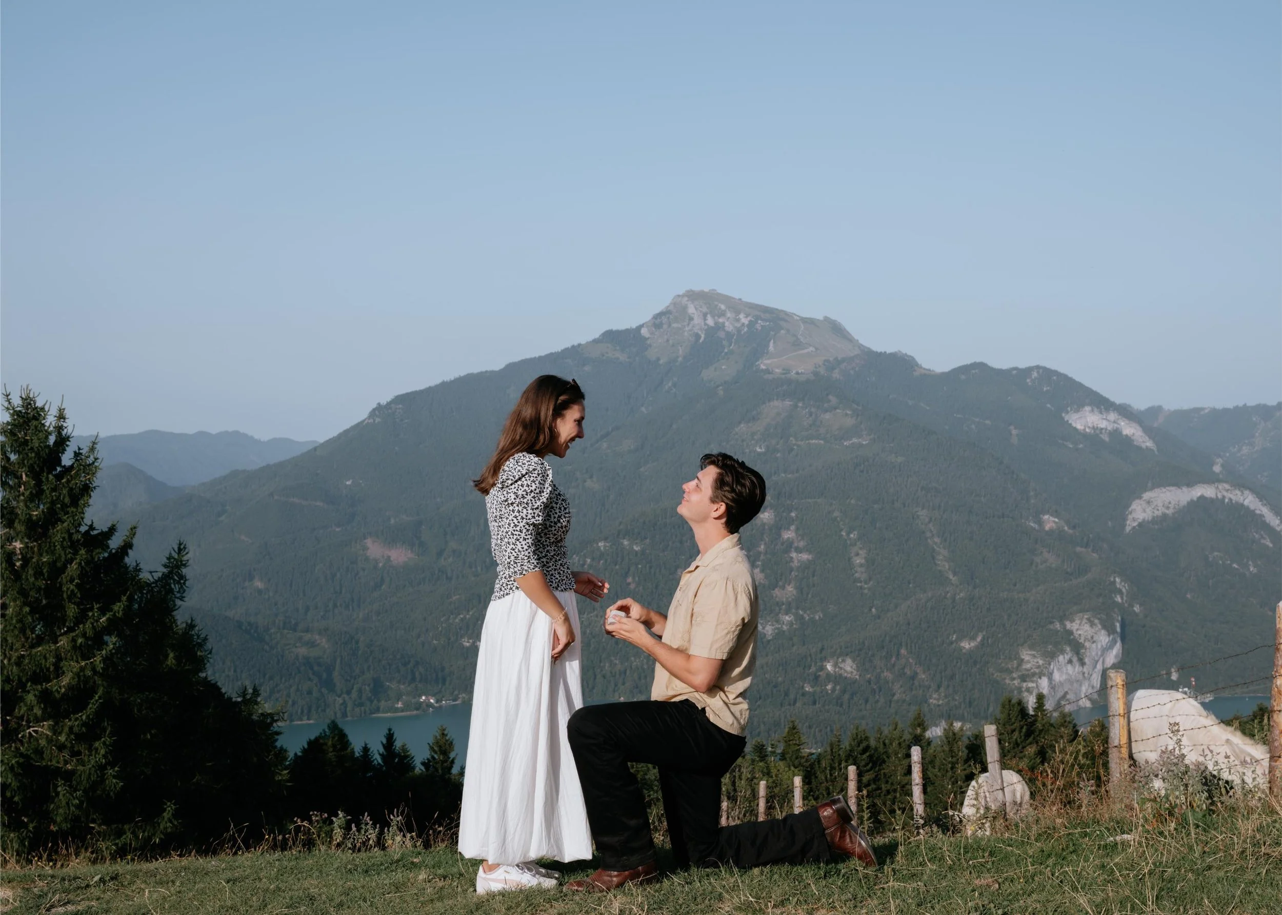 A man proposing marriage to a woman outdoors with mountains in the background.