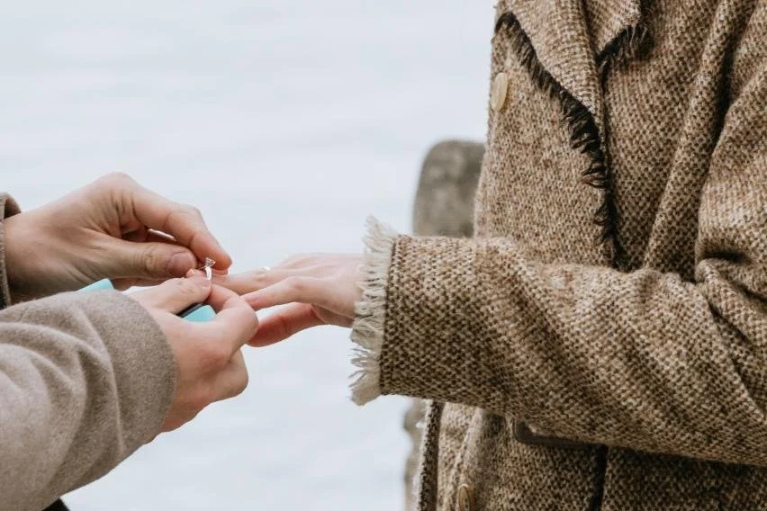Person handing a ring and a small box to another person during a wedding or proposal outdoors.