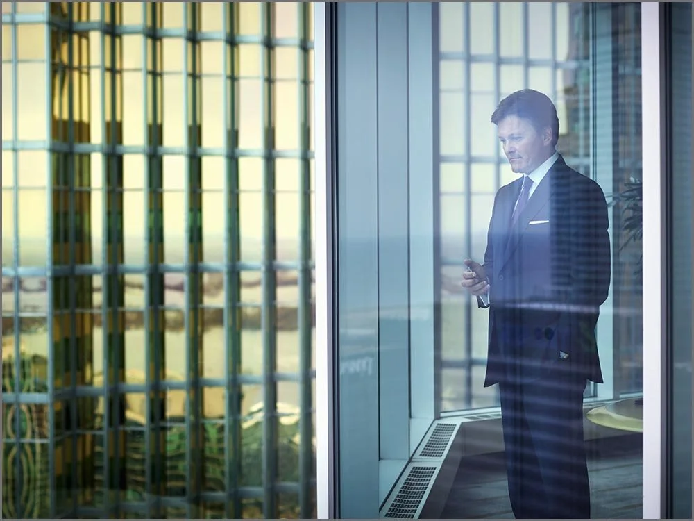 corporate lifestyle man with cellphone looking out of office tower.jpg
