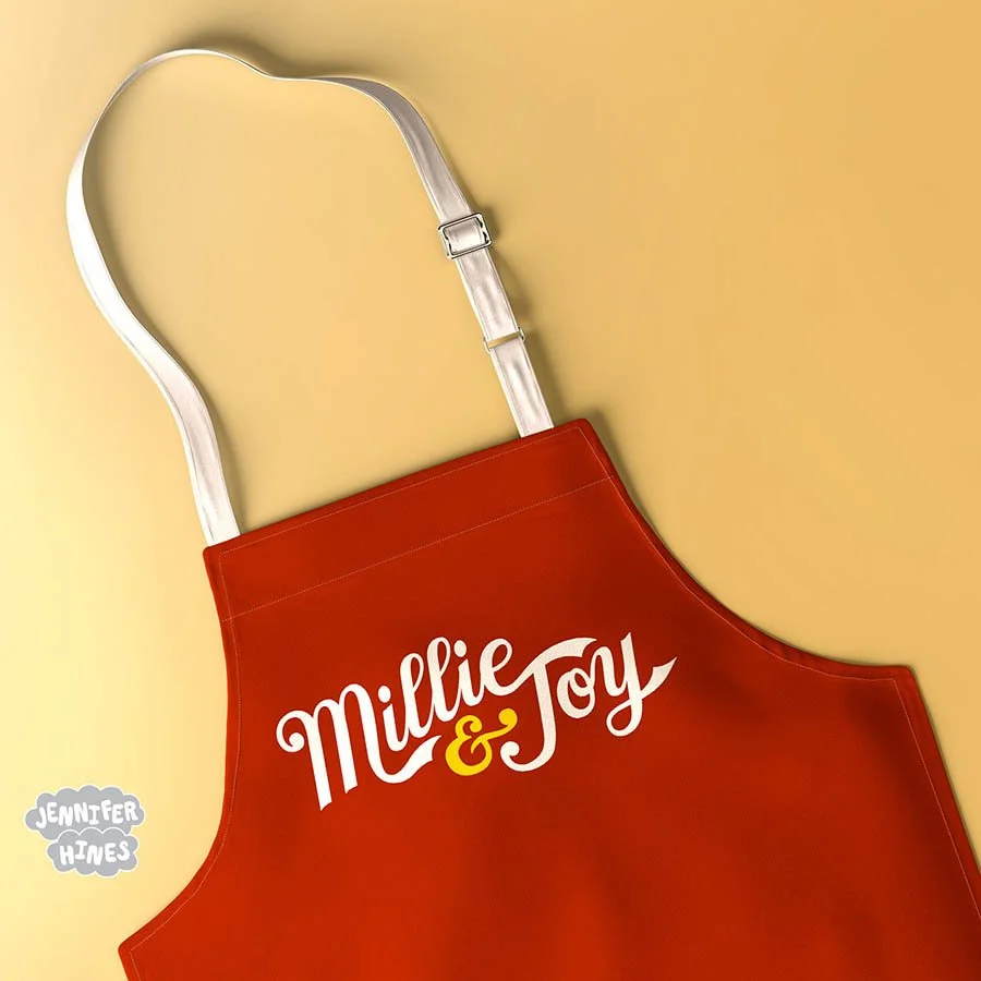 Image of a burgandy apron with a baking company logo Millie and Joy on a golden background