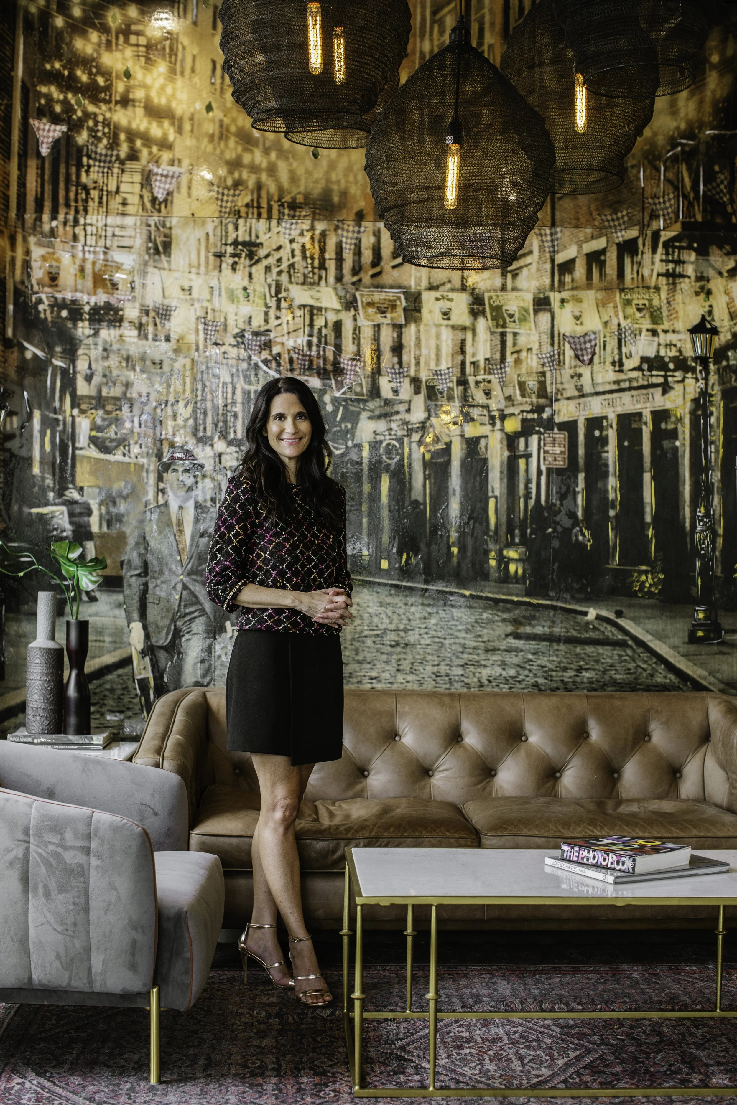 Madeleine Perez standing in a polished Los Angeles interior with a mural wall, sofa, and warm lighting.