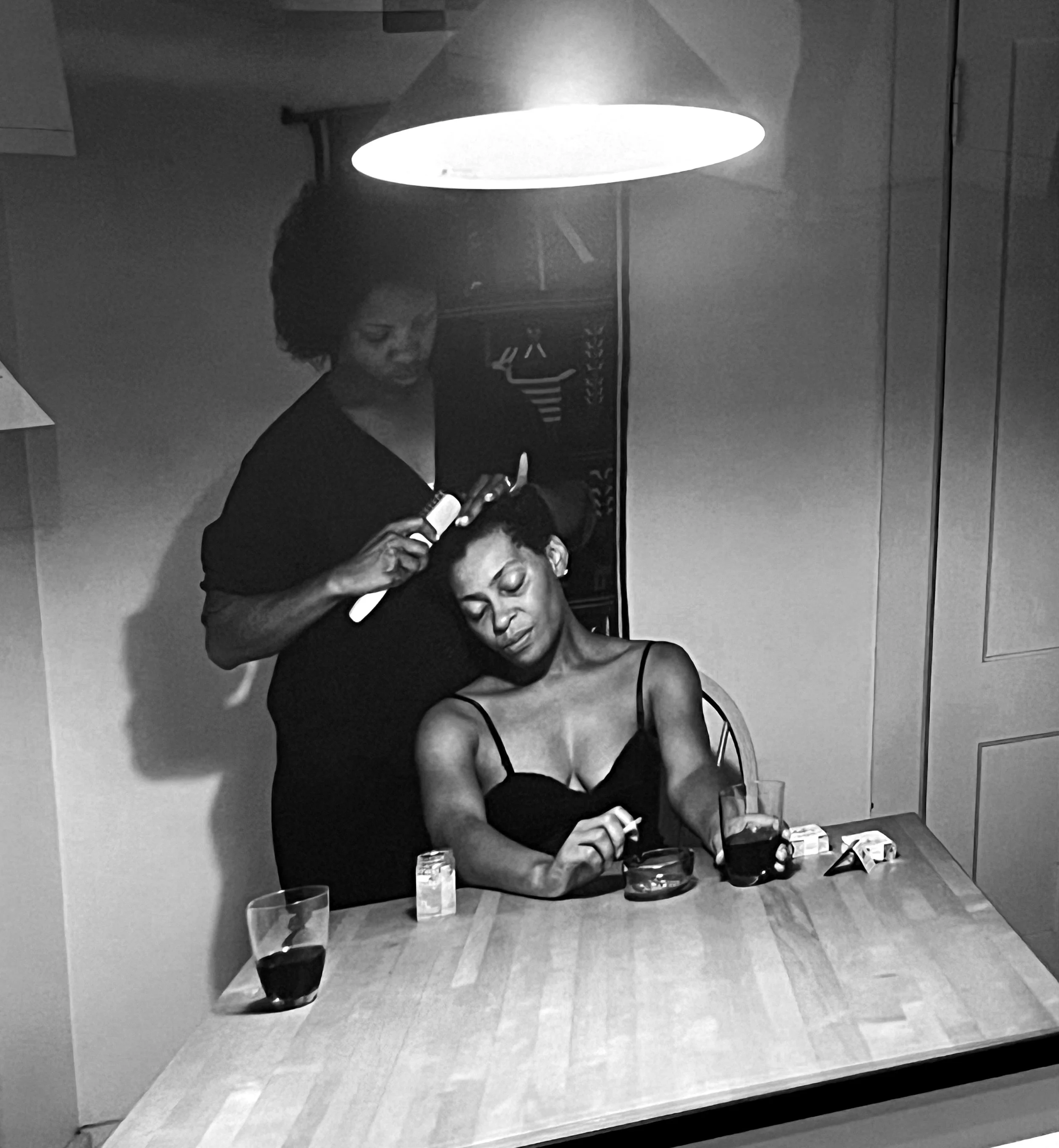 Two women at table. One is brishing the others hair tenderly