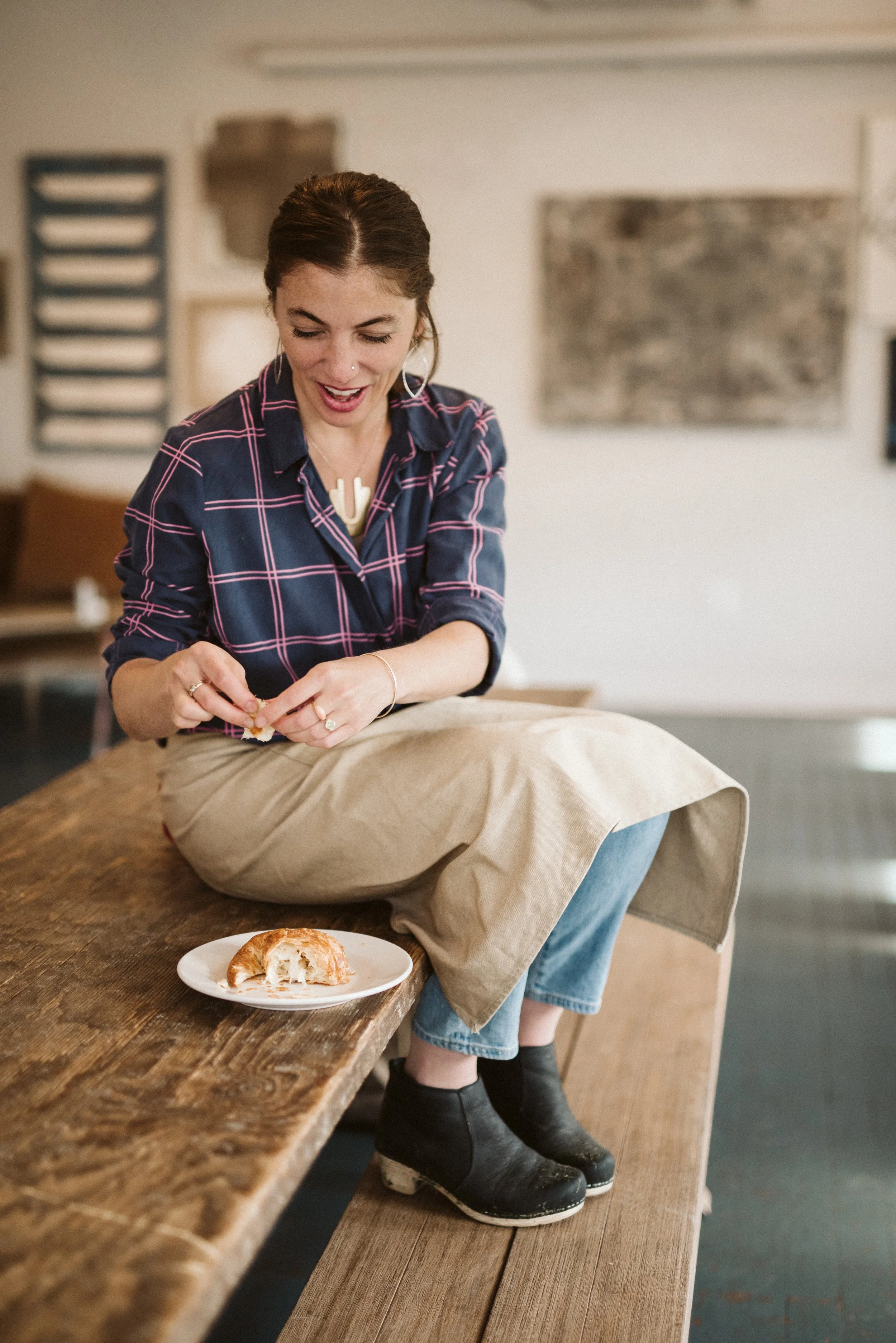 woman sitting atop a table eating croissant