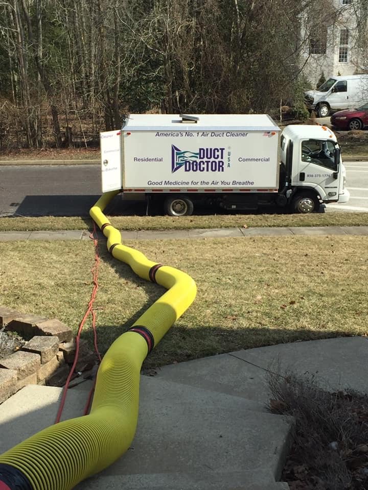 Long yellow vacuum hose connecting the Duct Doctor truck to a building across the grounds