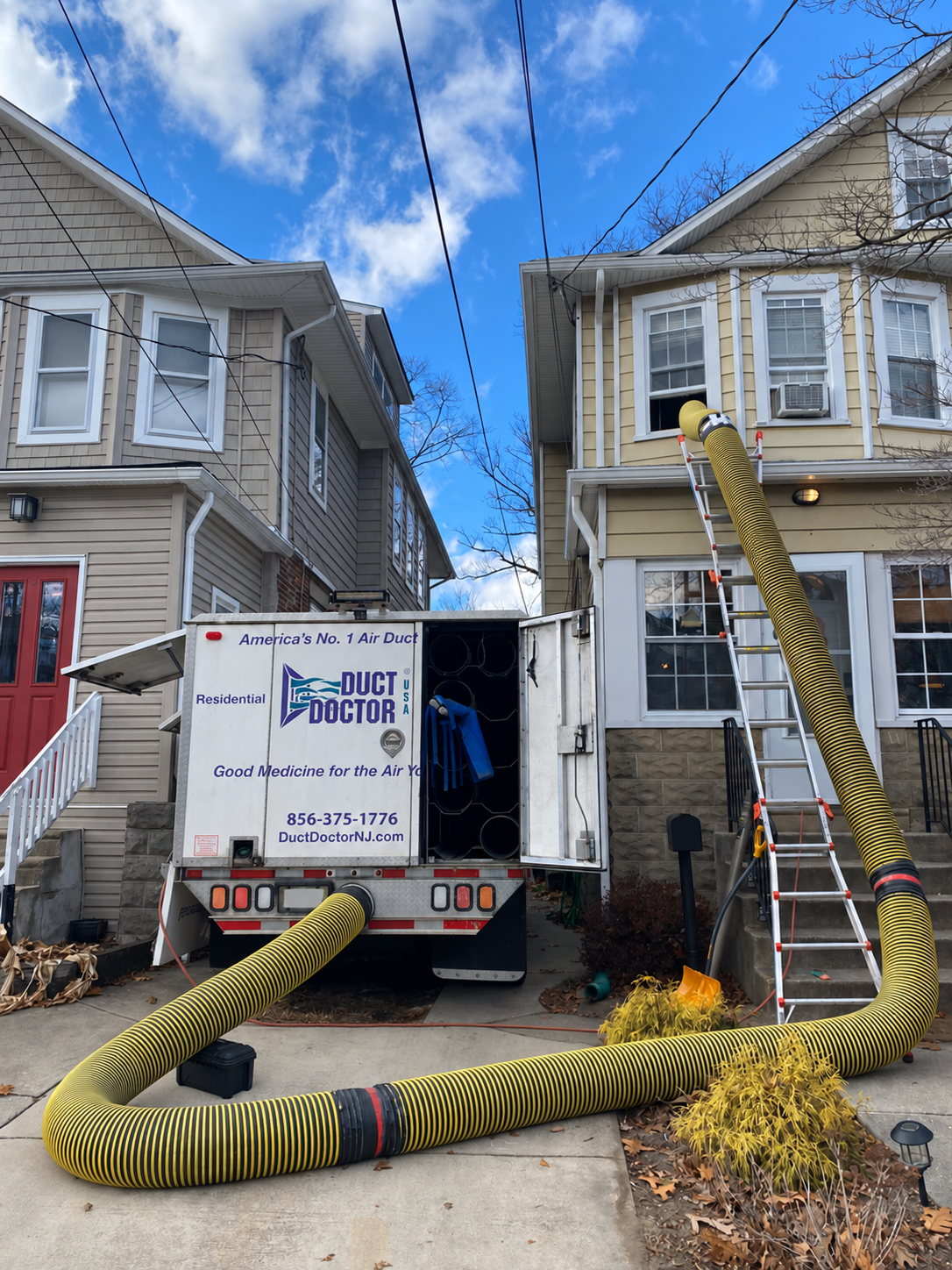 Duct Doctor truck and large vacuum hose routed to an upstairs window