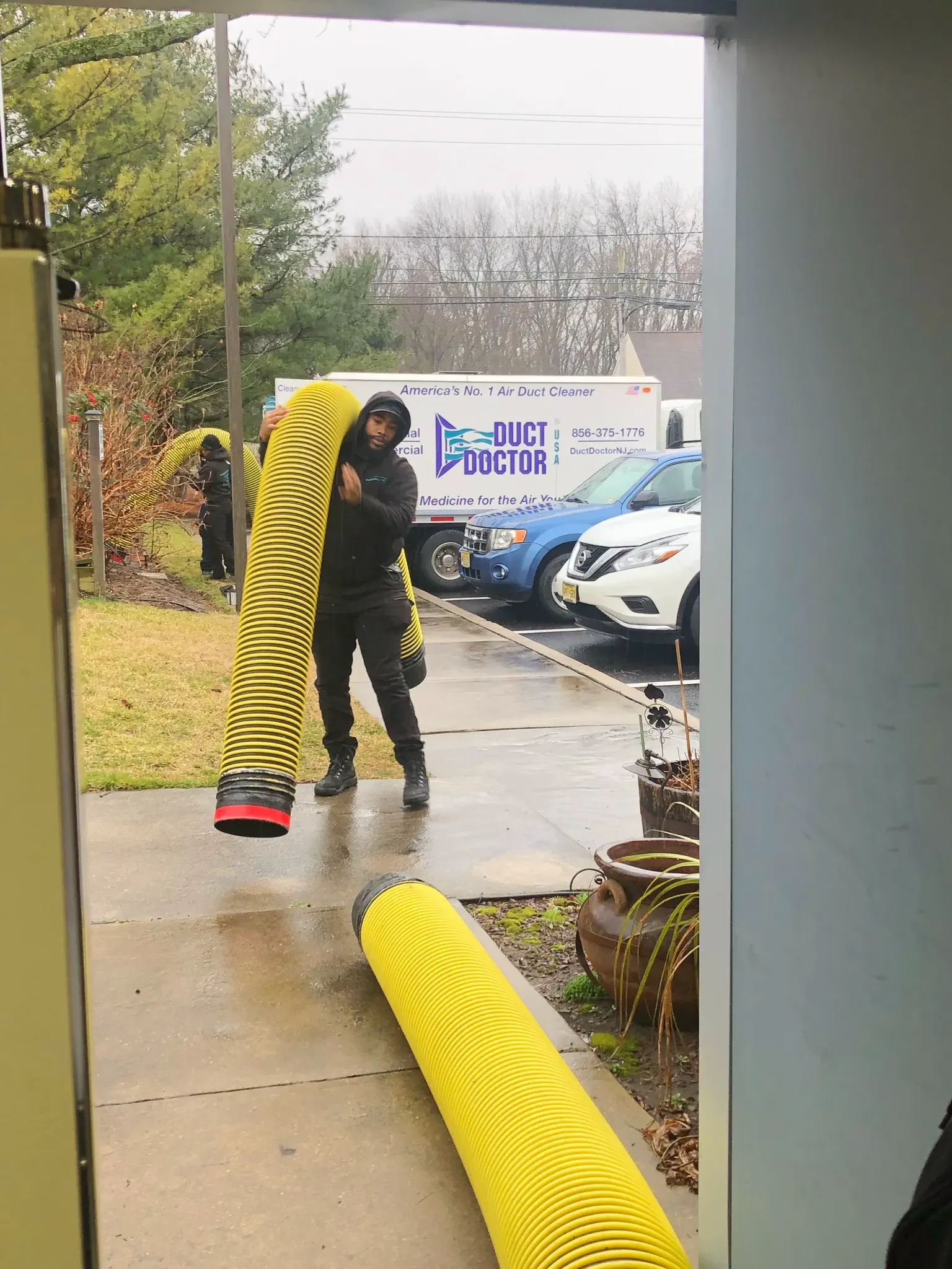 Duct Doctor technician carrying the yellow vacuum hose from the truck to a home HVAC system.