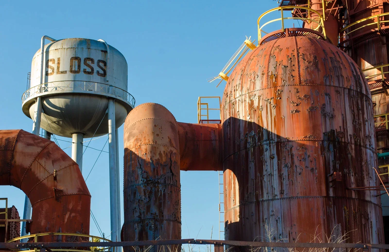 Rusted industrial blast furnaces and steel tanks at Sloss Furnaces National Historic Landmark in Birmingham, Alabama, photographed against a clear blue sky, showcasing historic steel mill infrastructure and industrial heritage.