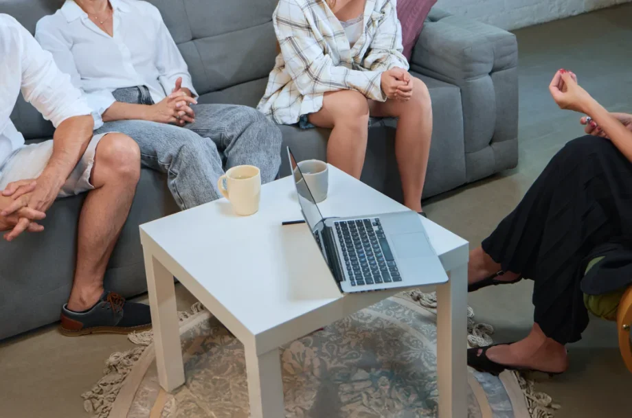 Family counseling session with multiple family members seated together on a sofa during a guided discussion with a licensed therapist in a professional office setting.