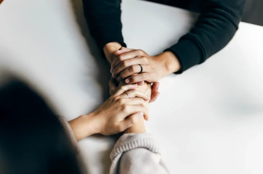 Couples counseling session showing two partners holding hands during a supportive conversation with a licensed therapist.