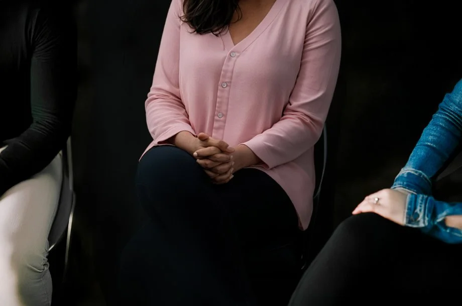 Group counseling session with several adults seated in a group, participating in a facilitated discussion in a supportive therapy setting.