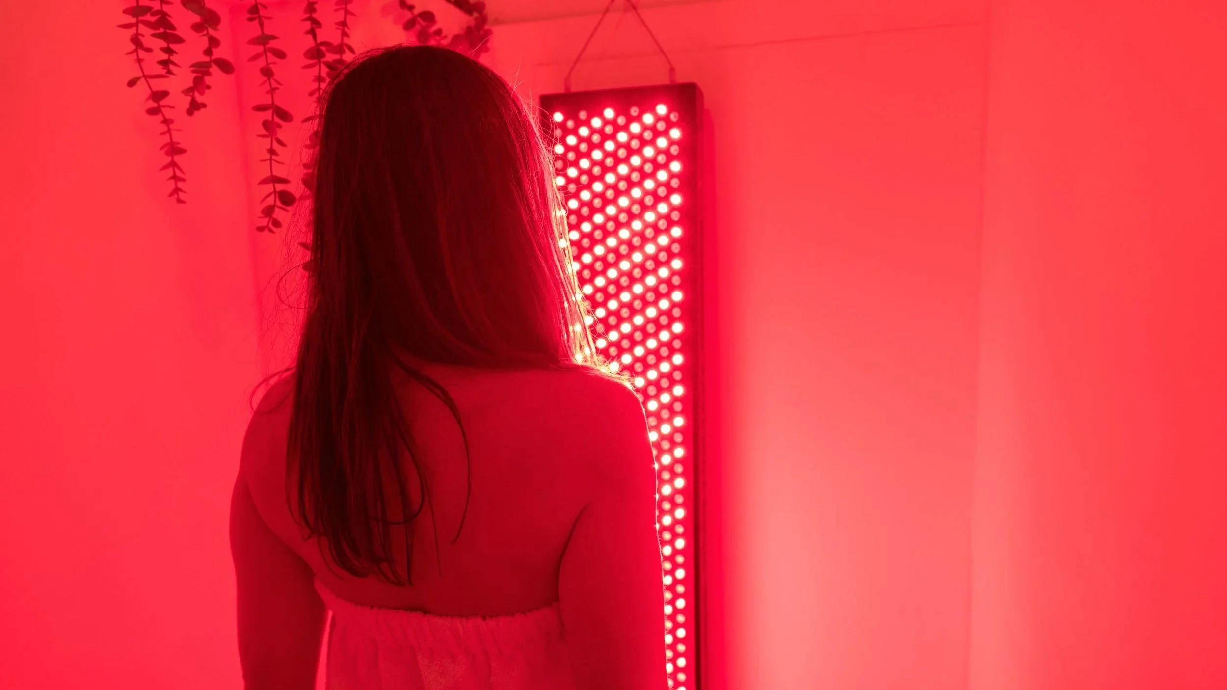 Person standing in front of a red light therapy panel in a calm recovery environment, supporting circulation and physiological recovery