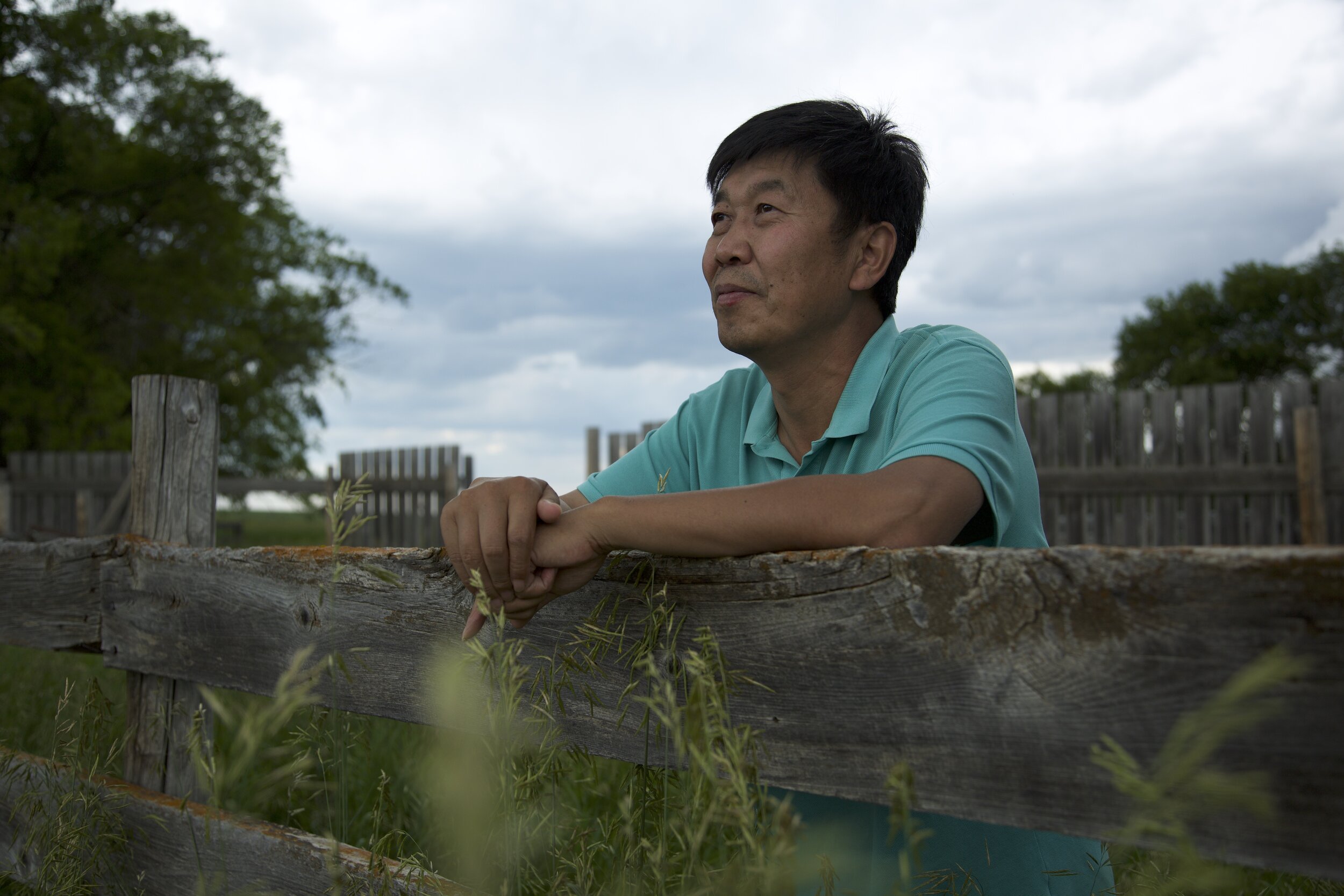 Farmland - David Fu leaning on a fence, with the future of his farm uncertain.jpg