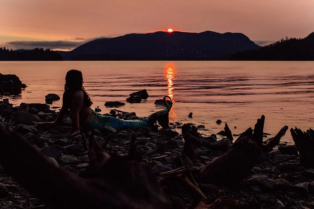 mermaid-sits-on-rocky-coast-in-juneau-as-sun-sets.jpg