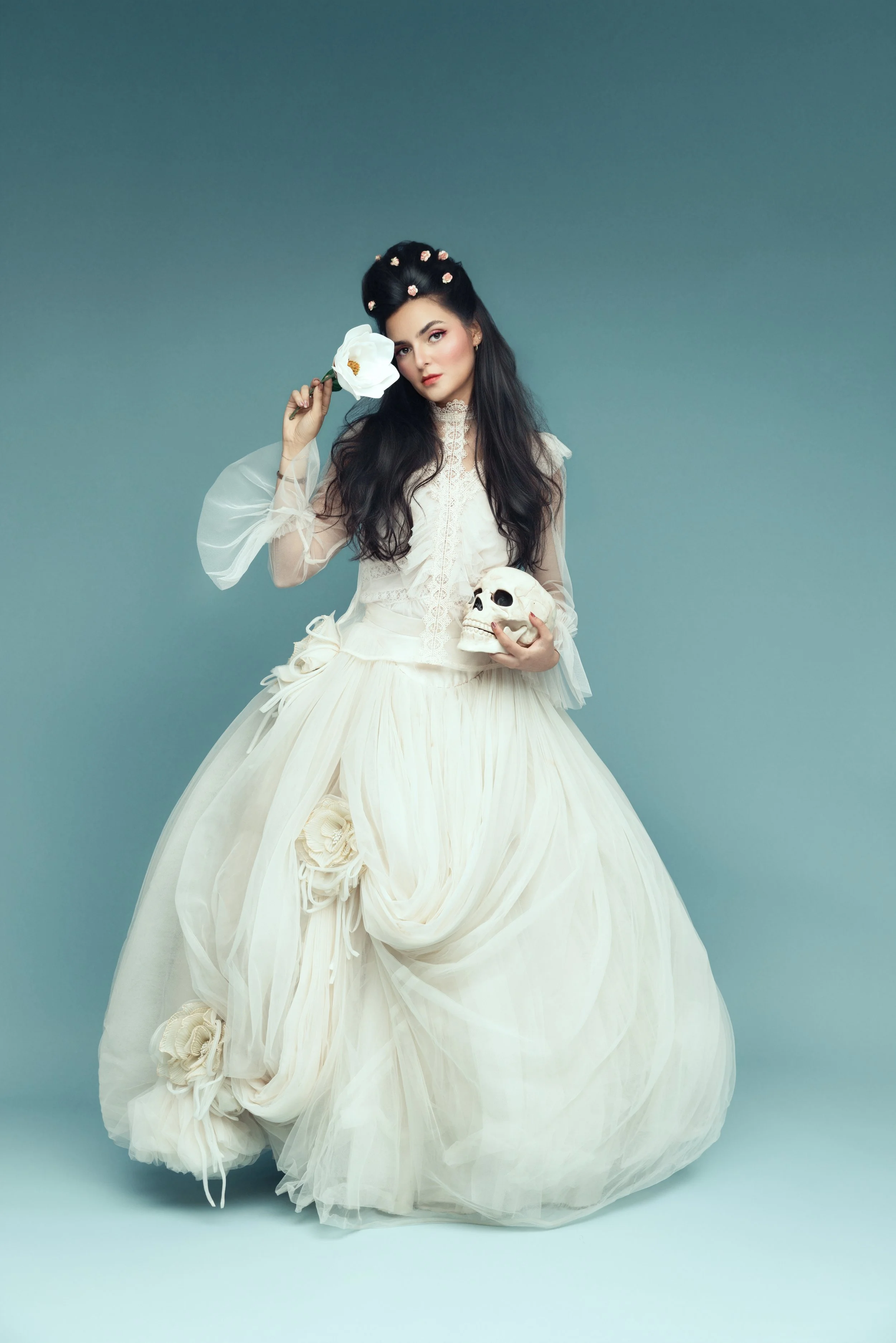 Young woman in a white ball gown holding a skull on a teal backdrop, gothic fine art storytelling portrait McAllen Texas