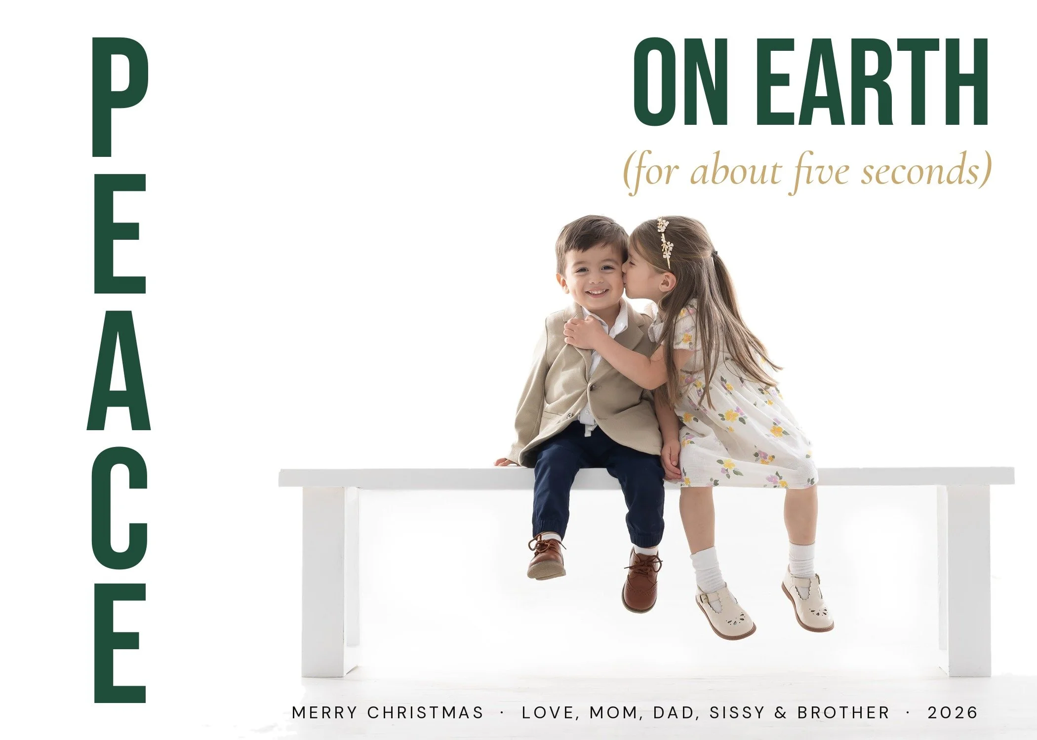 Custom Christmas card with PEACE stacked vertically in green beside a little girl kissing her brother's cheek on a white bench, McAllen TX children's photographer