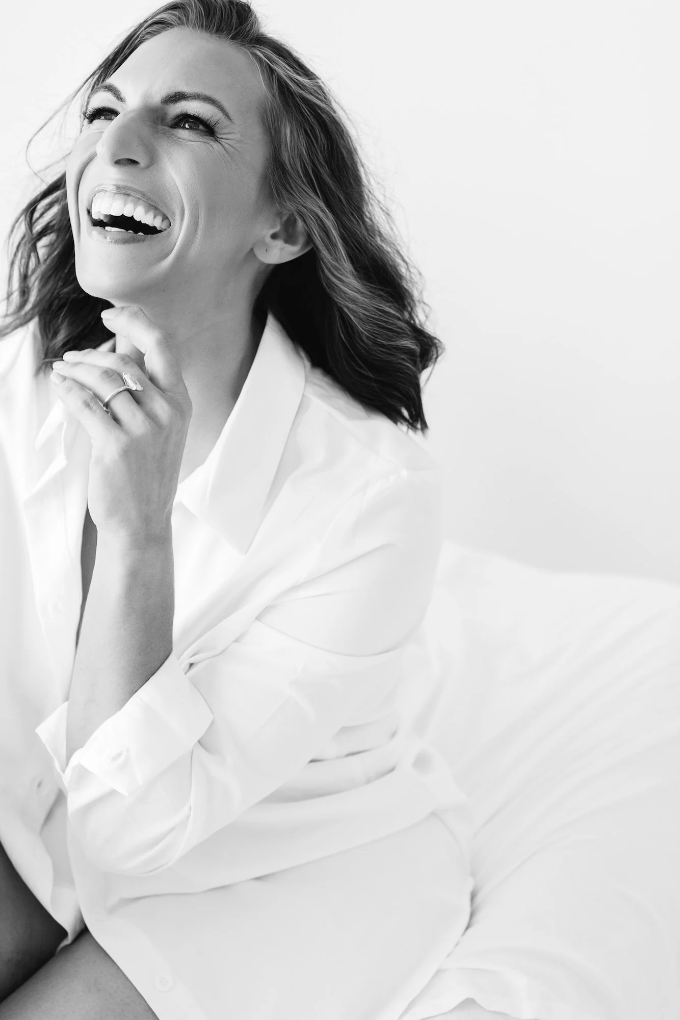 Woman laughing joyfully in a white button-down during a McAllen boudoir session with Nicole Gates Photography