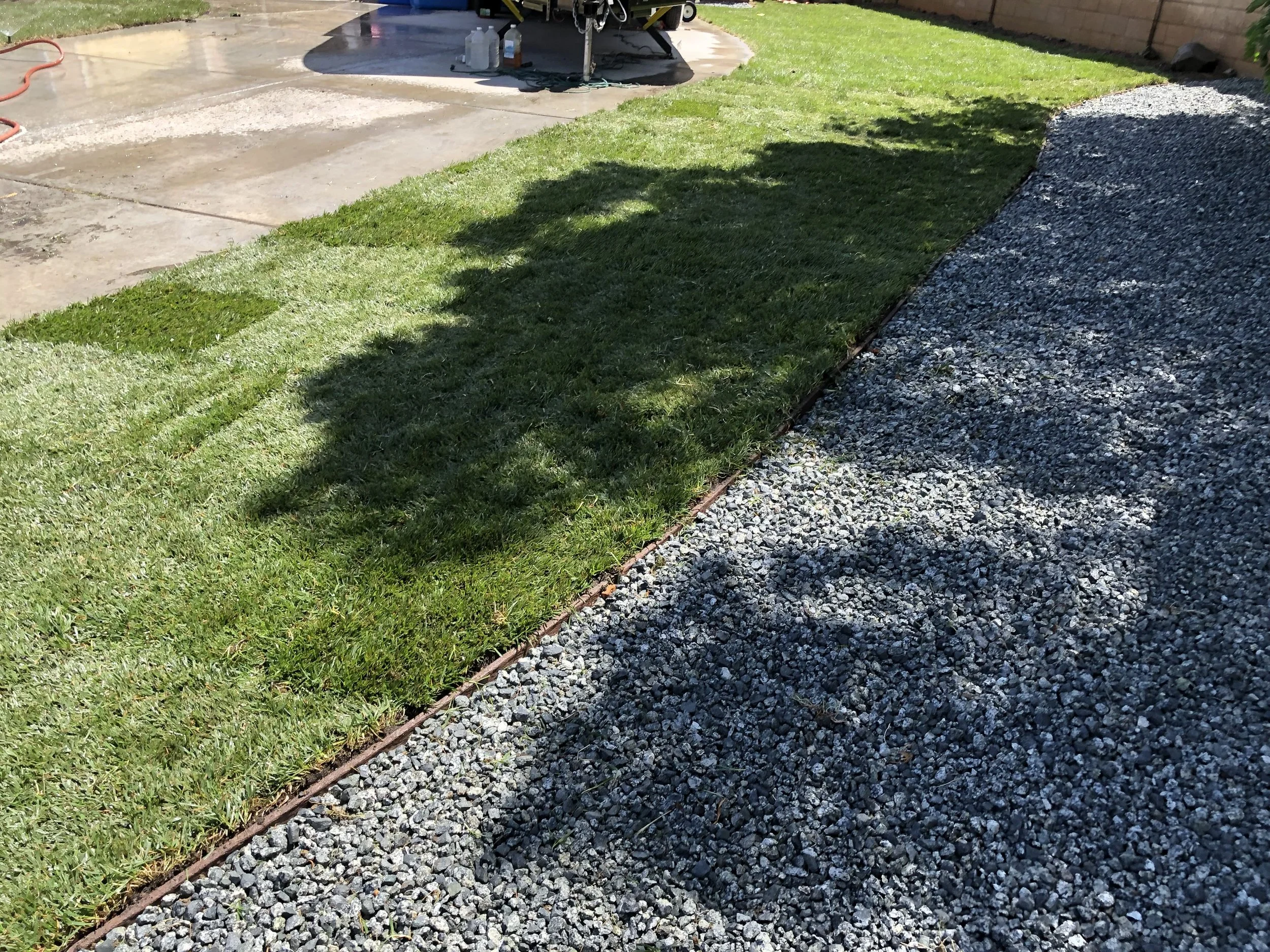 Freshly laid sod grass next to gravel path in a backyard, with part of a concrete patio visible in the background.