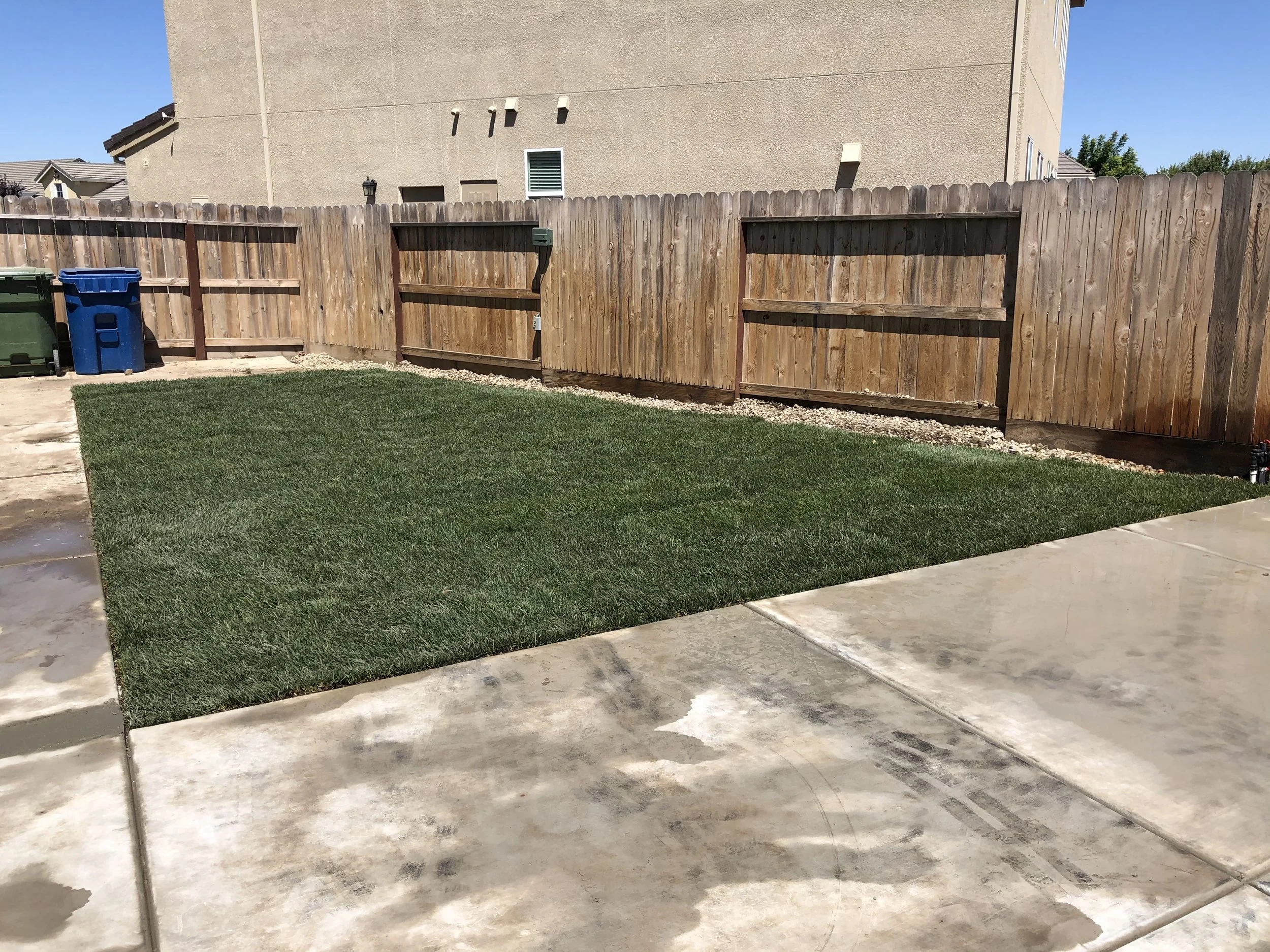 Backyard with a small patch of green grass, a wooden fence, and a concrete patio area.