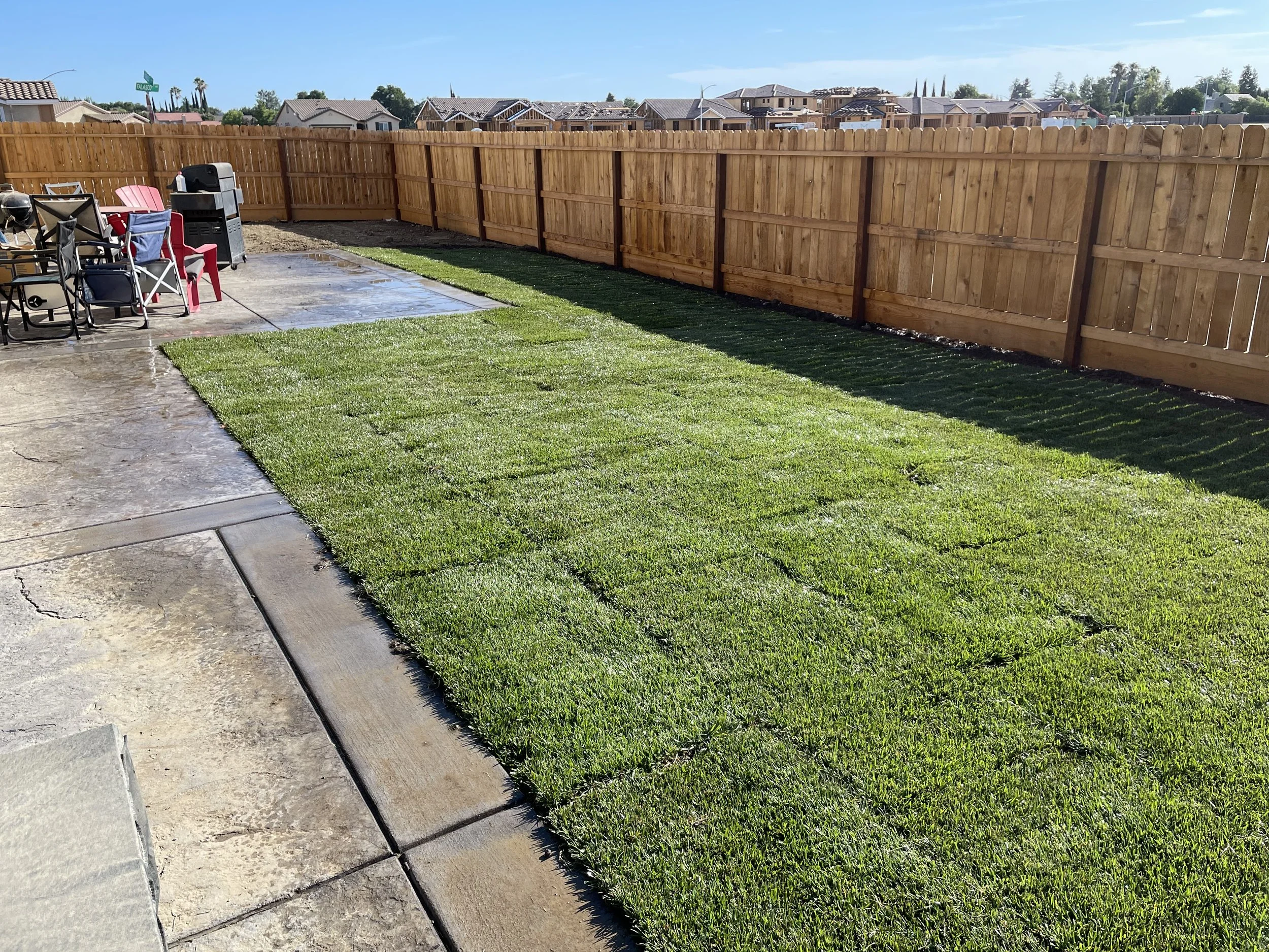 Backyard with a green sod lawn, wooden privacy fence, and patio area with outdoor furniture and a barbecue grill.