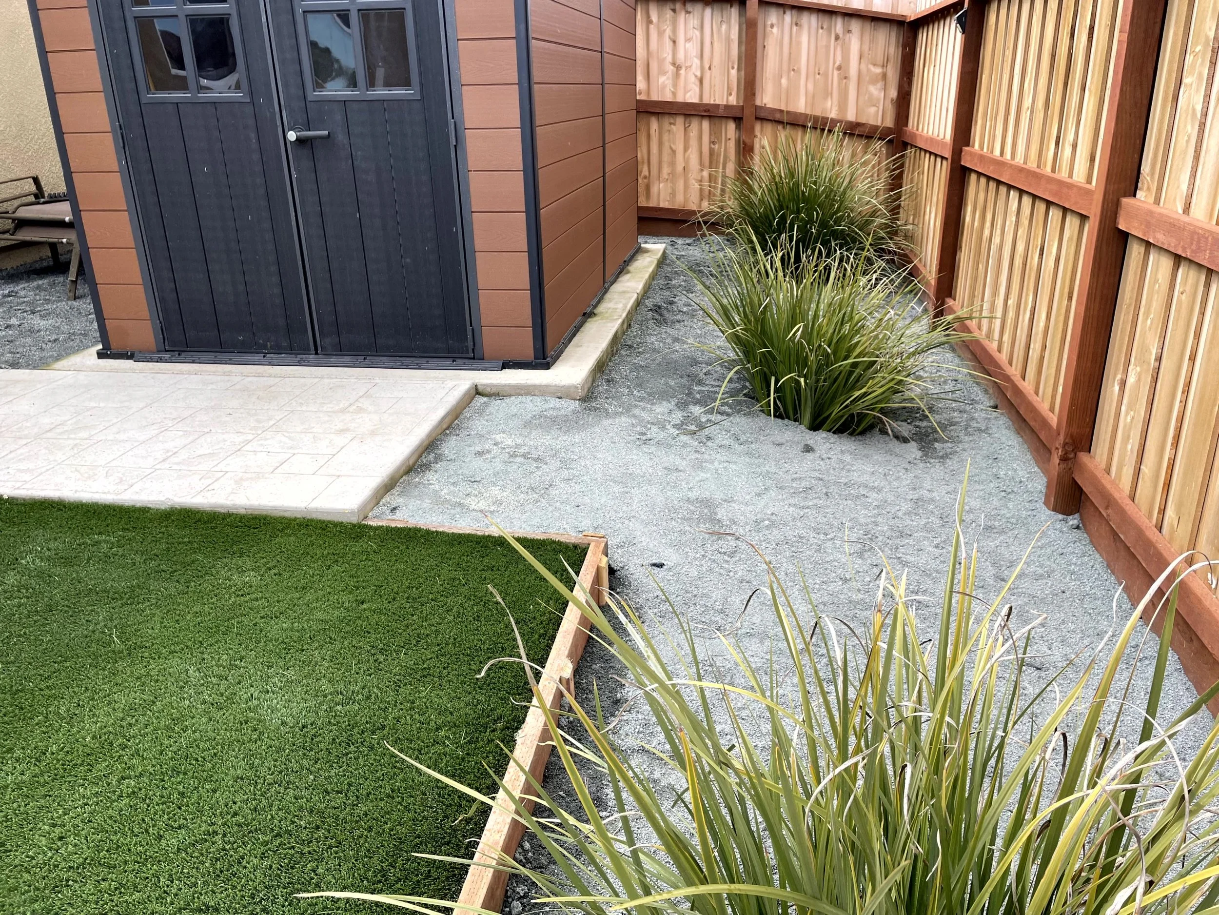 Backyard with a small shed, a green lawn, gravel pathway, and a wooden fence.