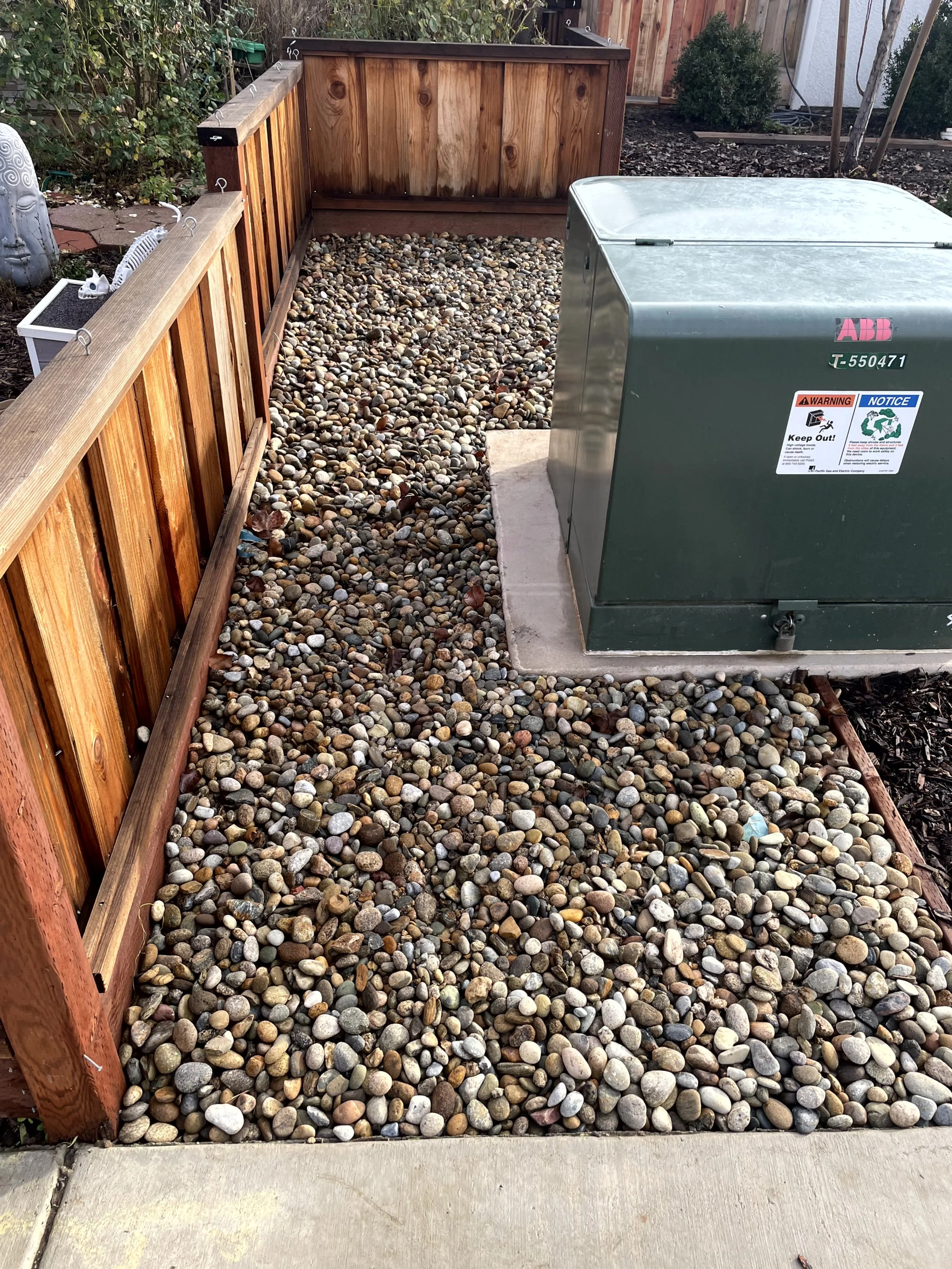 Garden area with a wooden fence, a gravel pathway, and a gray electrical transformer box.
