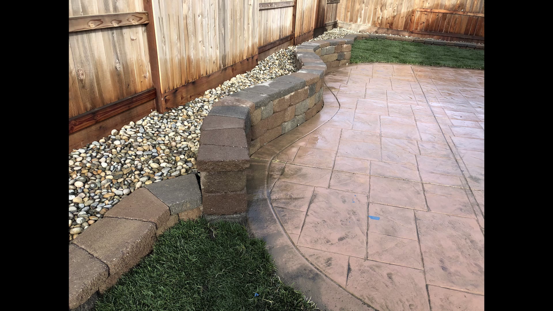 Backyard patio with stamped concrete, a curved brick wall, gravel bed, and a wooden fence.