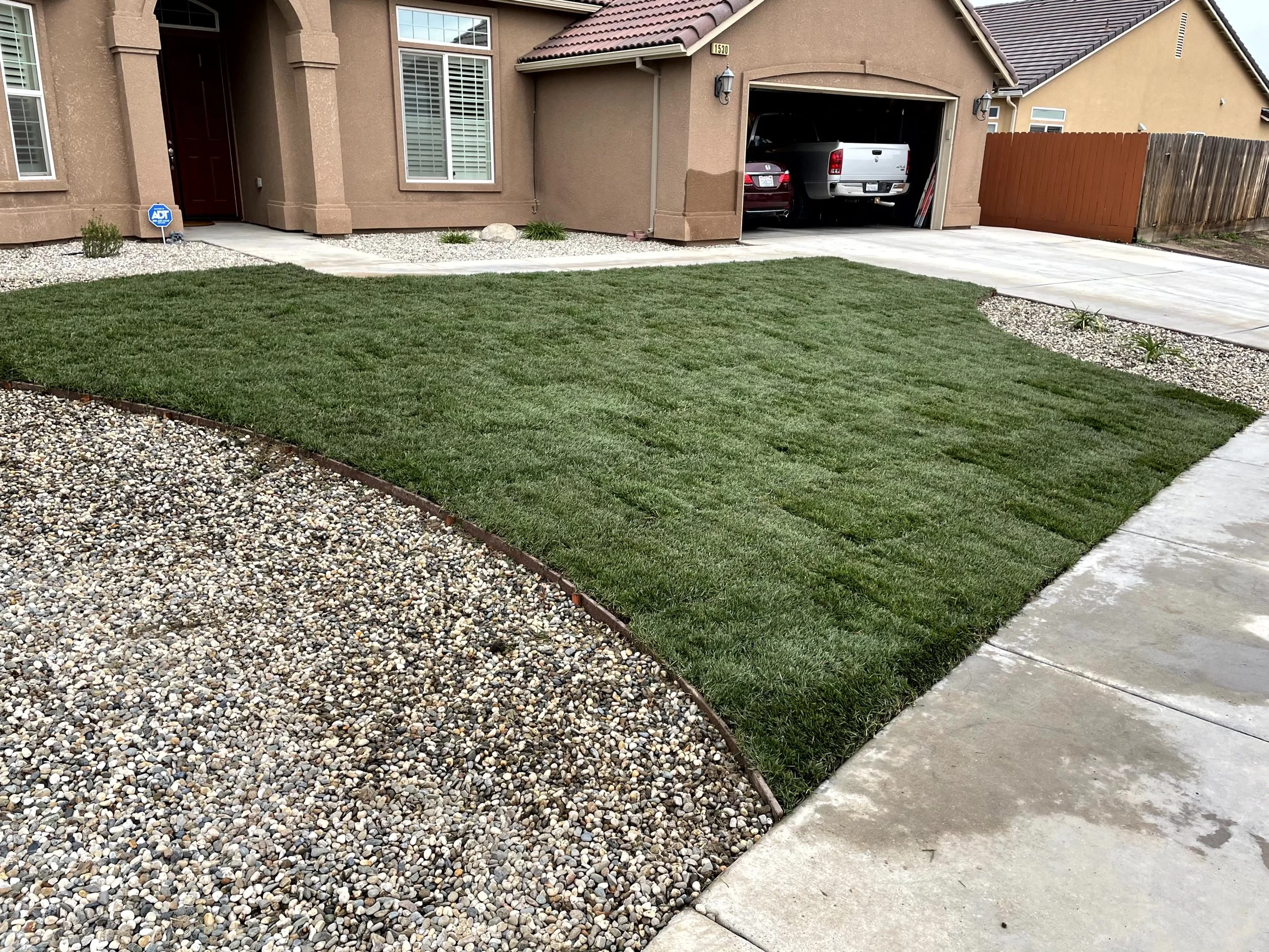 Front yard of a house with a well-maintained lawn, a pebble border, and a driveway leading to a two-car garage.