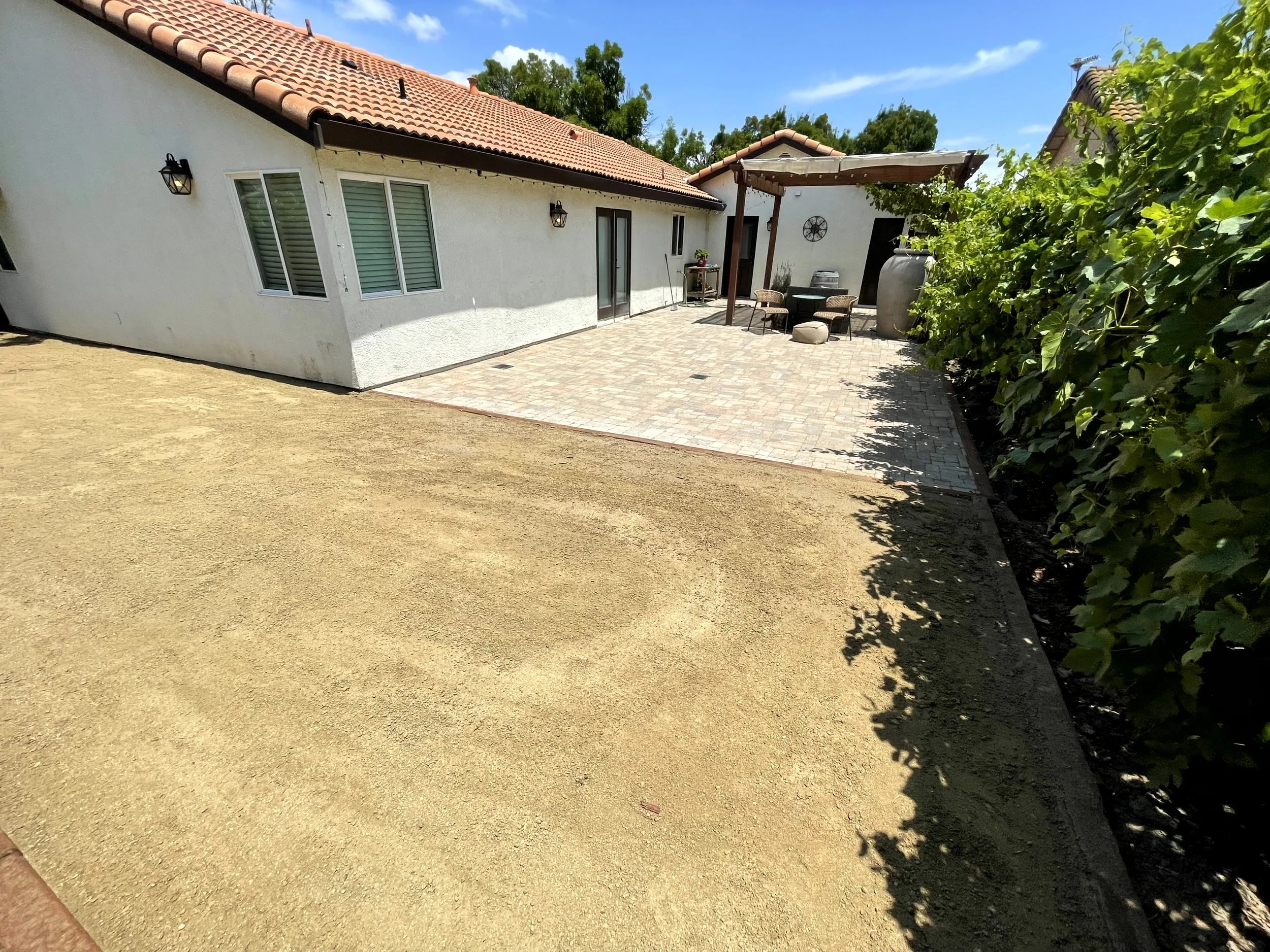 Backyard patio area with a small seating area, pavers, and a shaded corner with plants and outdoor decor
