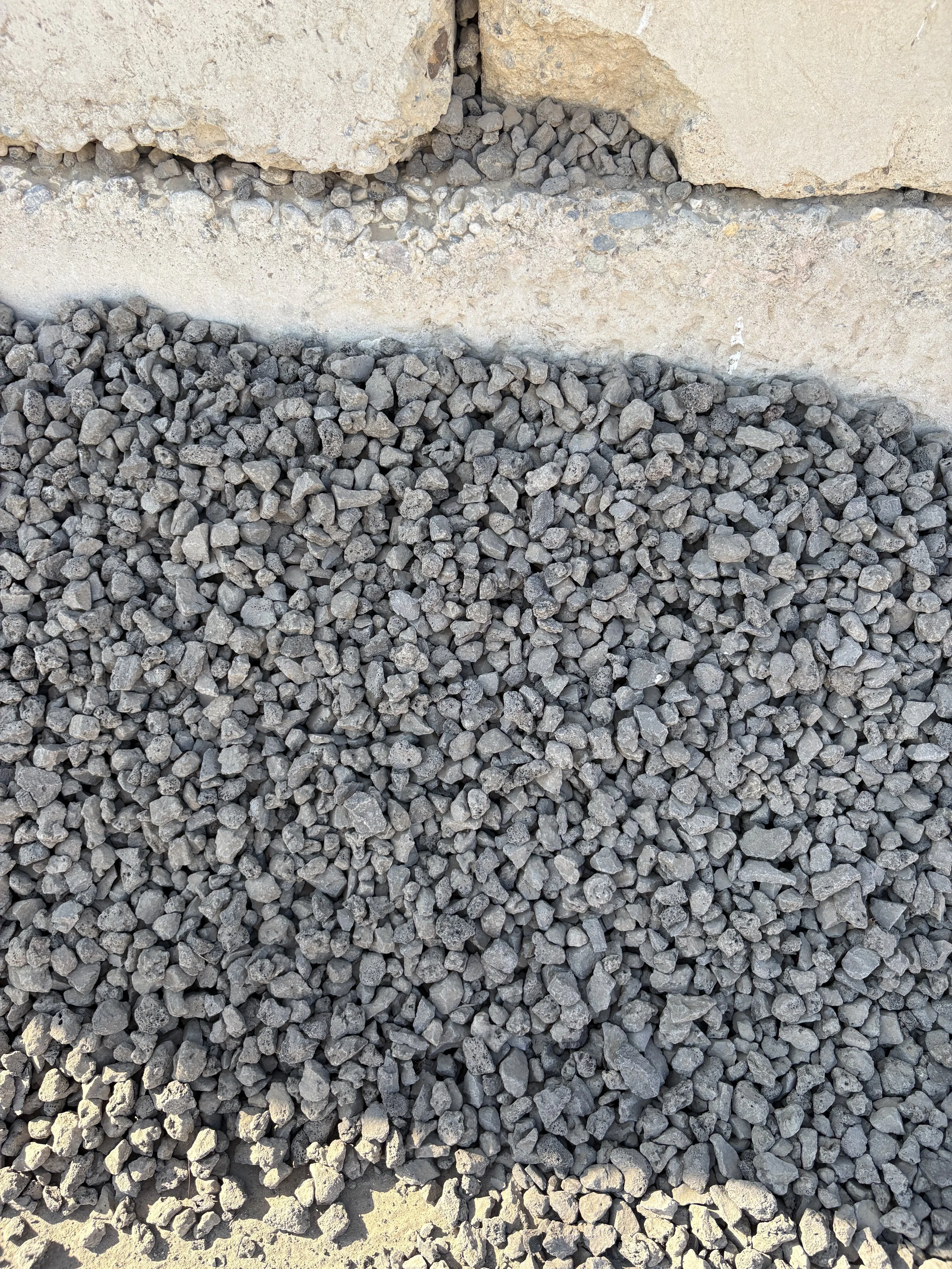 Close-up of small gray gravel stones on the ground next to a beige concrete or stone wall.