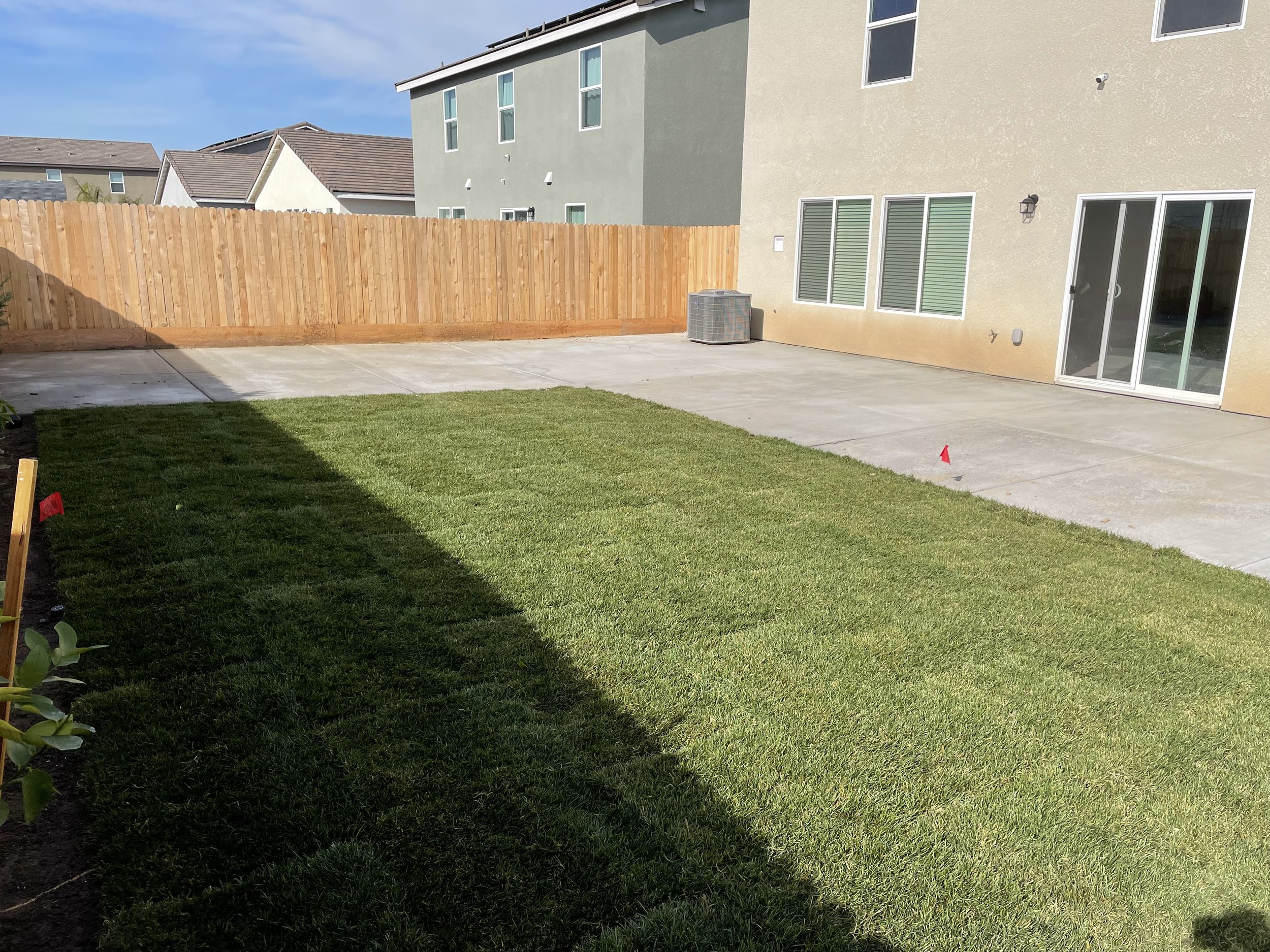 Backyard area with green grass, concrete patio, a wooden privacy fence, and house with sliding glass door and multiple windows.