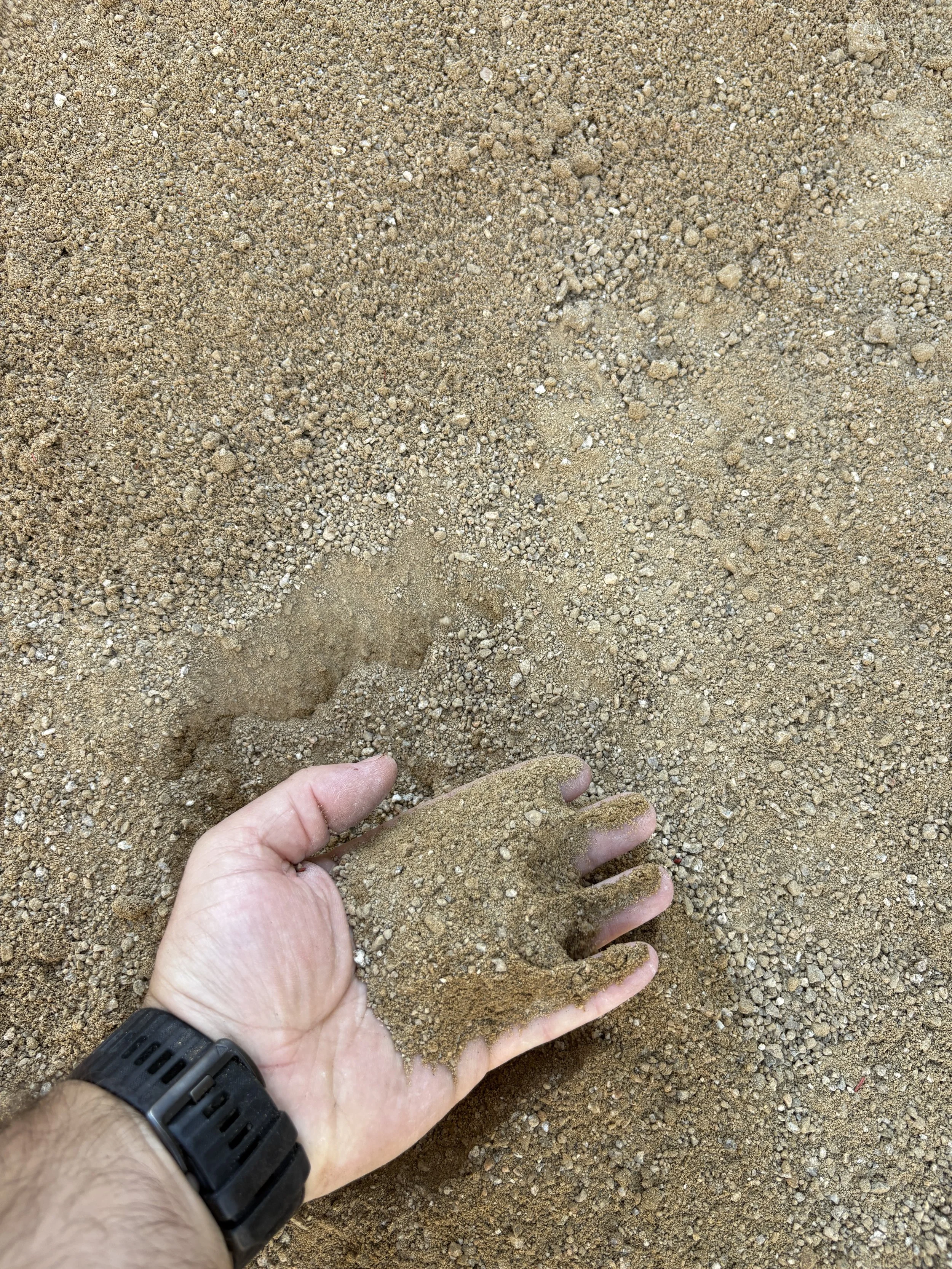 A person's hand is covered with sand and appears to be forming a shape like a small sculpture on a sandy beach.