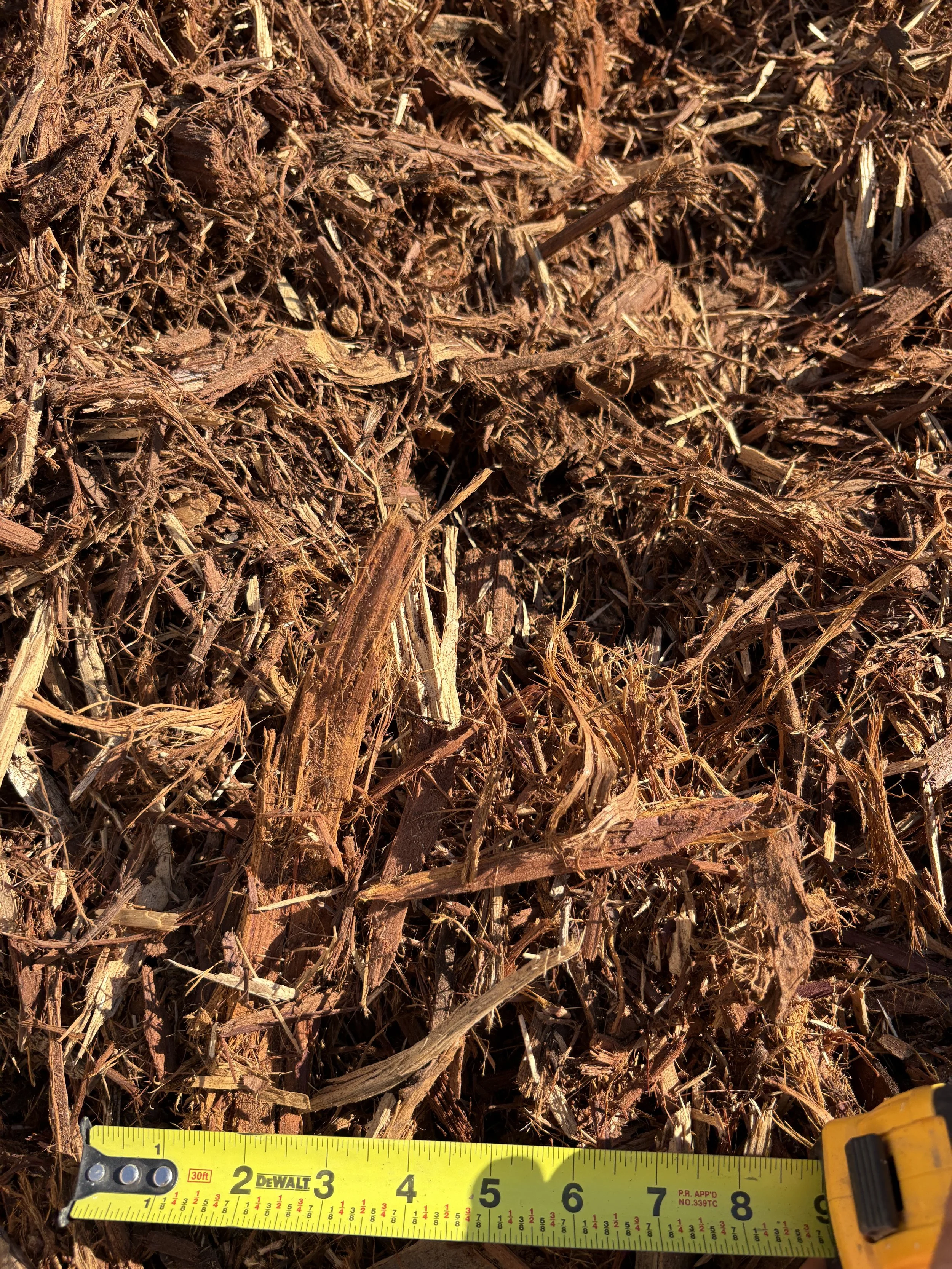 Close-up of shredded bark mulch with a yellow measuring tape below, showing measurements in inches.