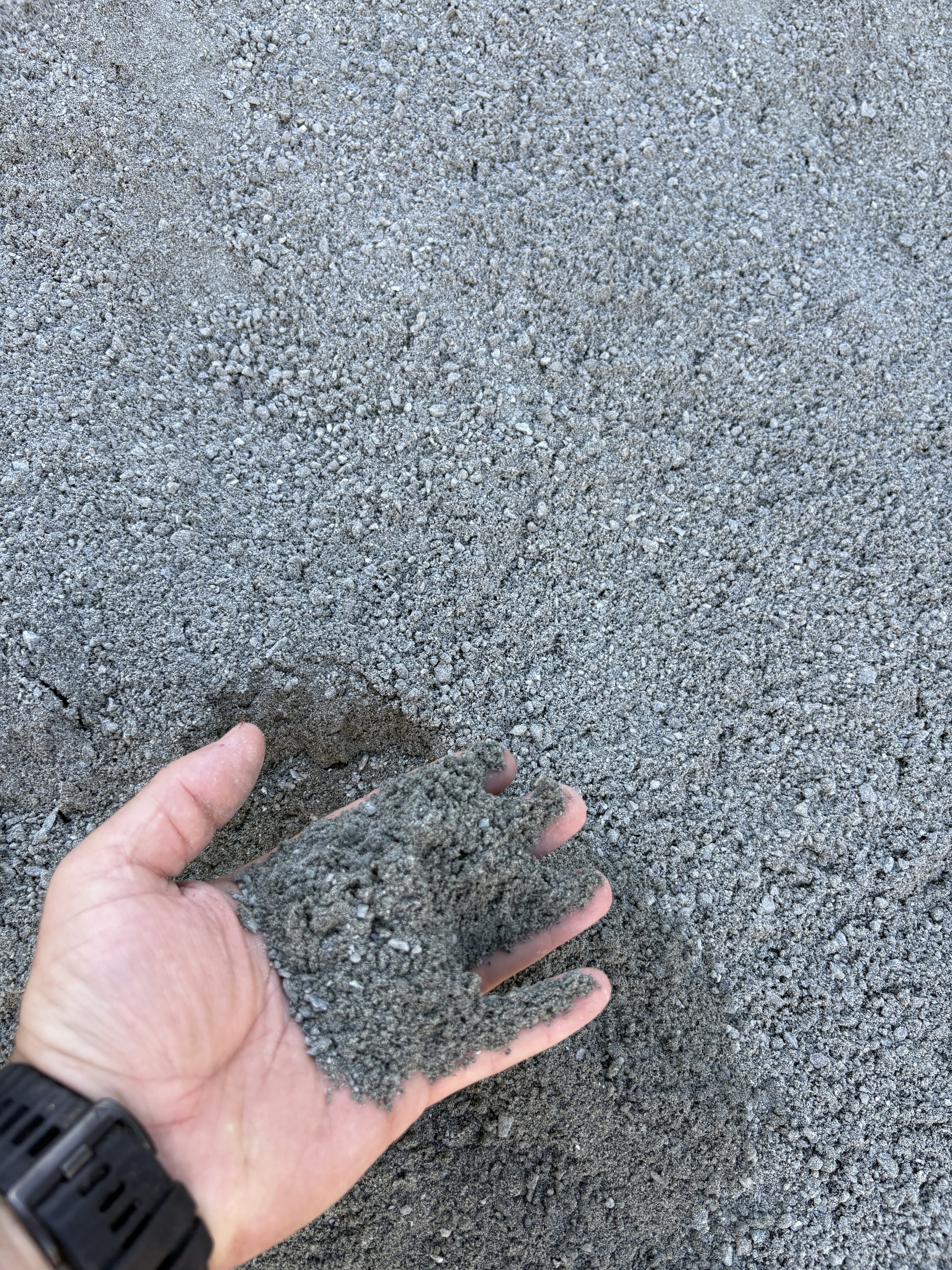 Hand holding a mound of gray sand or gravel over a surface of gray sand or gravel