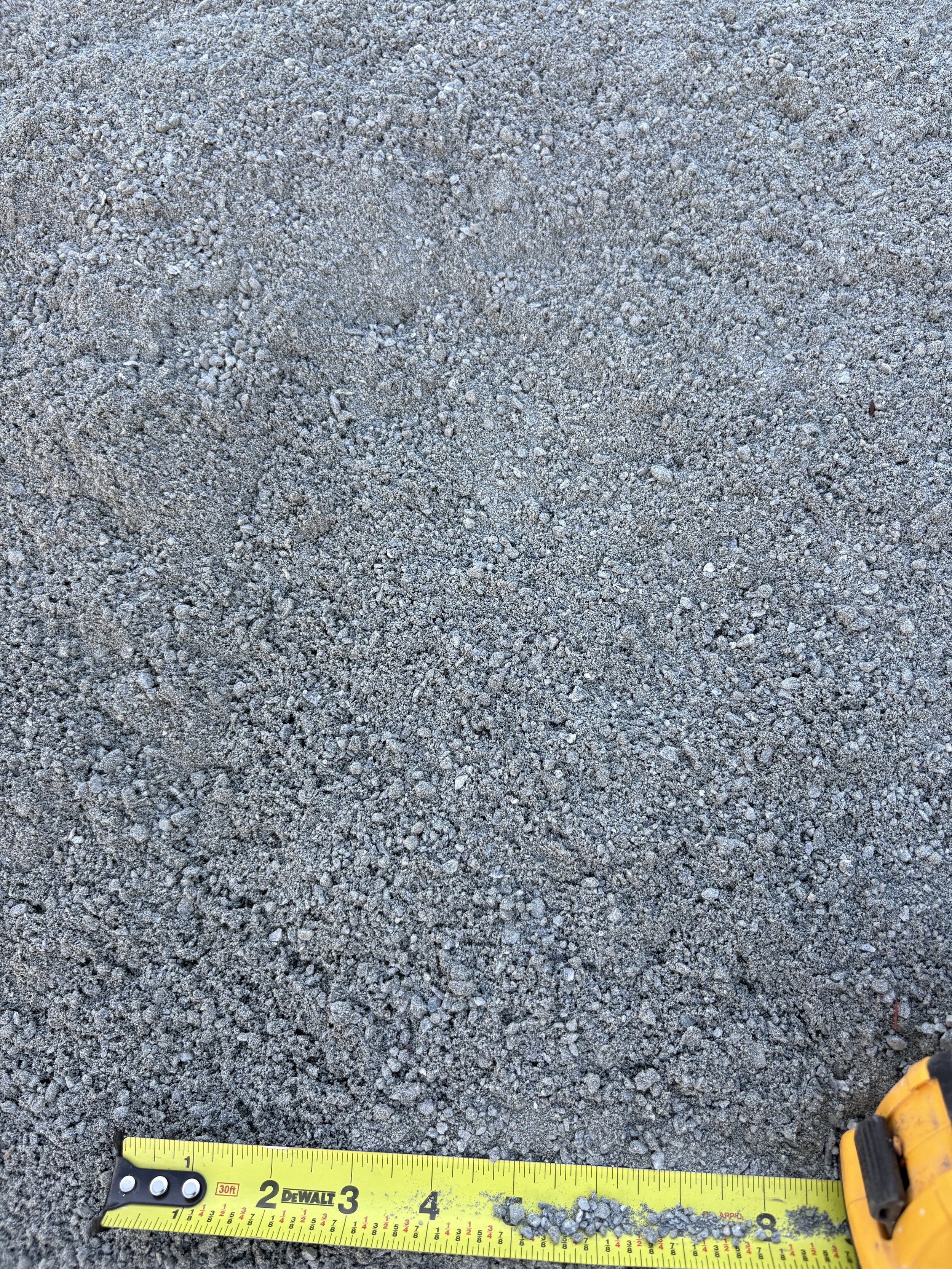 Close-up of gray gravel surface with a yellow measuring tape showing approximately 8 inches at the bottom right corner.